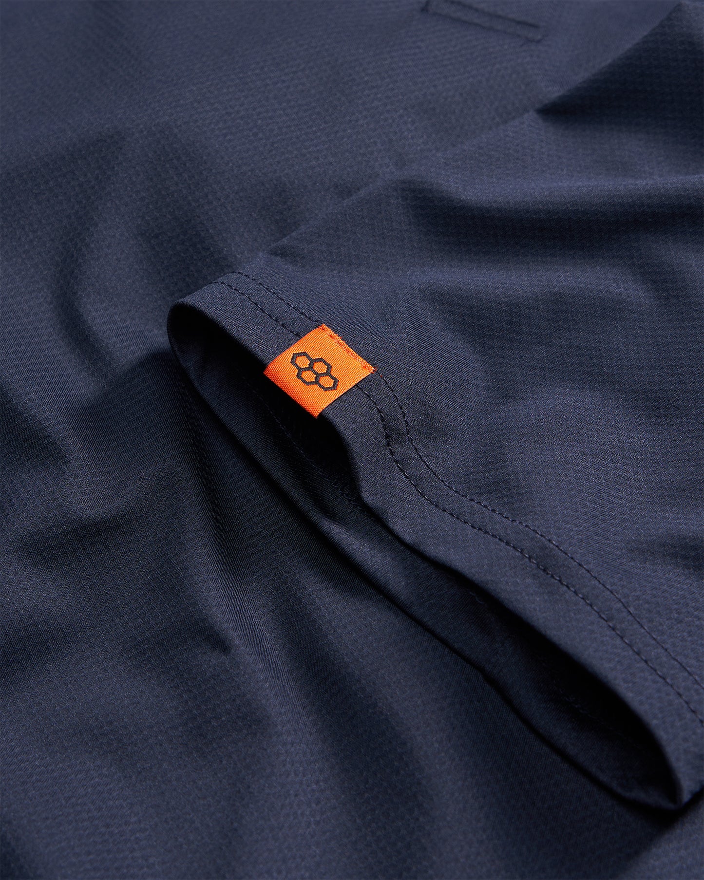 This image features a close-up of a dark navy fabric with an orange tag highlighting a textured surface and detailed stitching