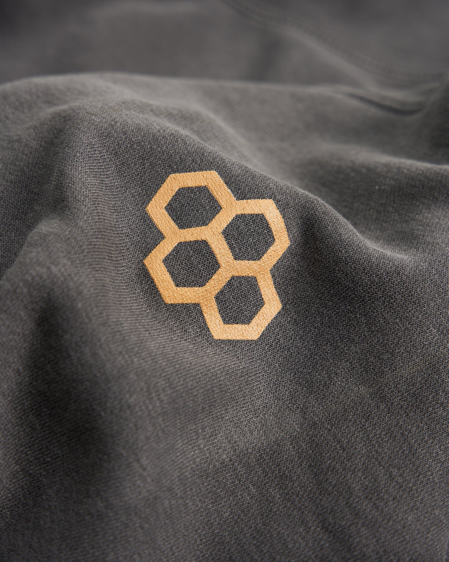 A close-up view of a dark fabric displaying an embossed honeycomb logo in a light golden color