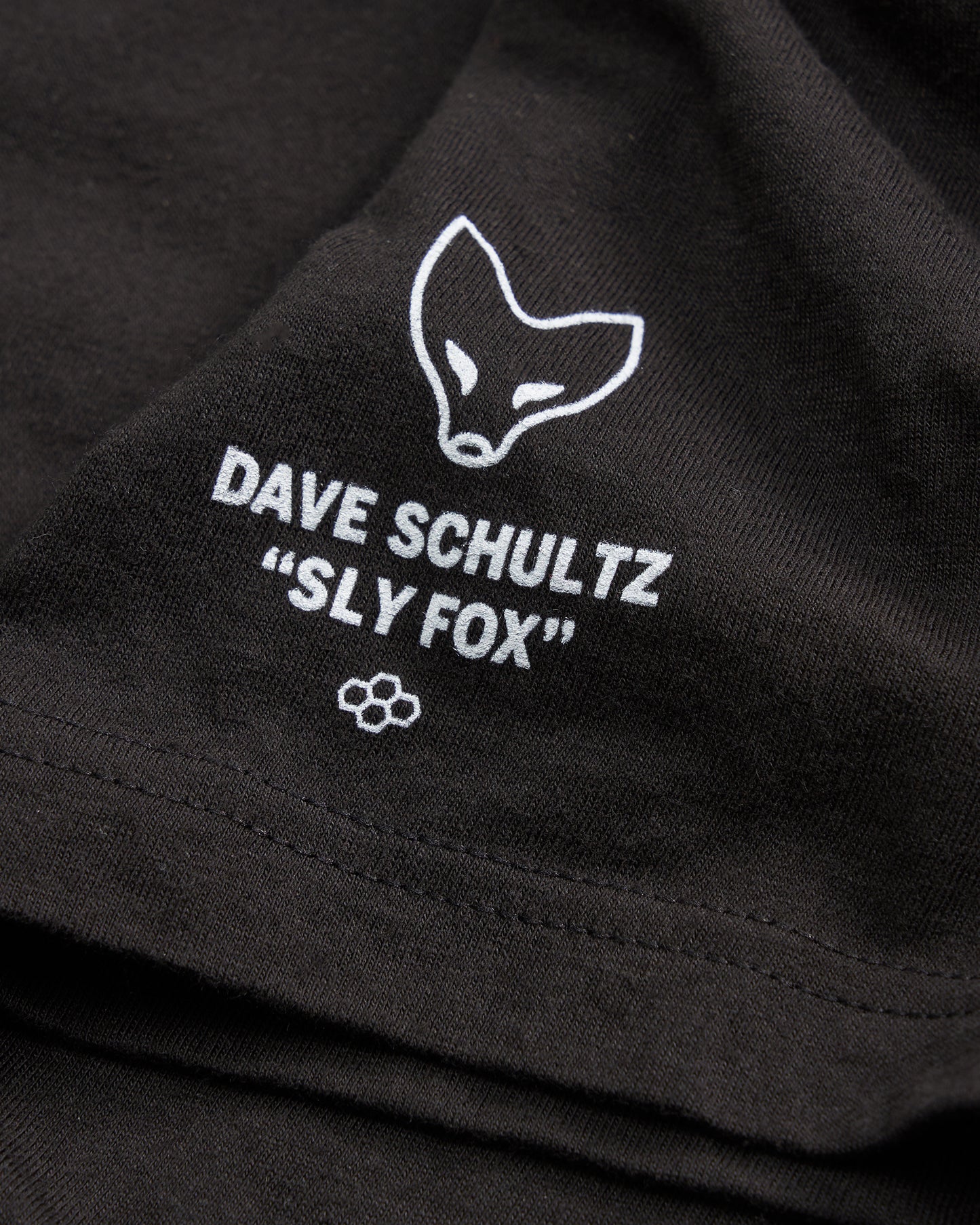 A close-up of a black fabric featuring white printed text and a fox illustration associated with Dave Schultzs Sly Fox