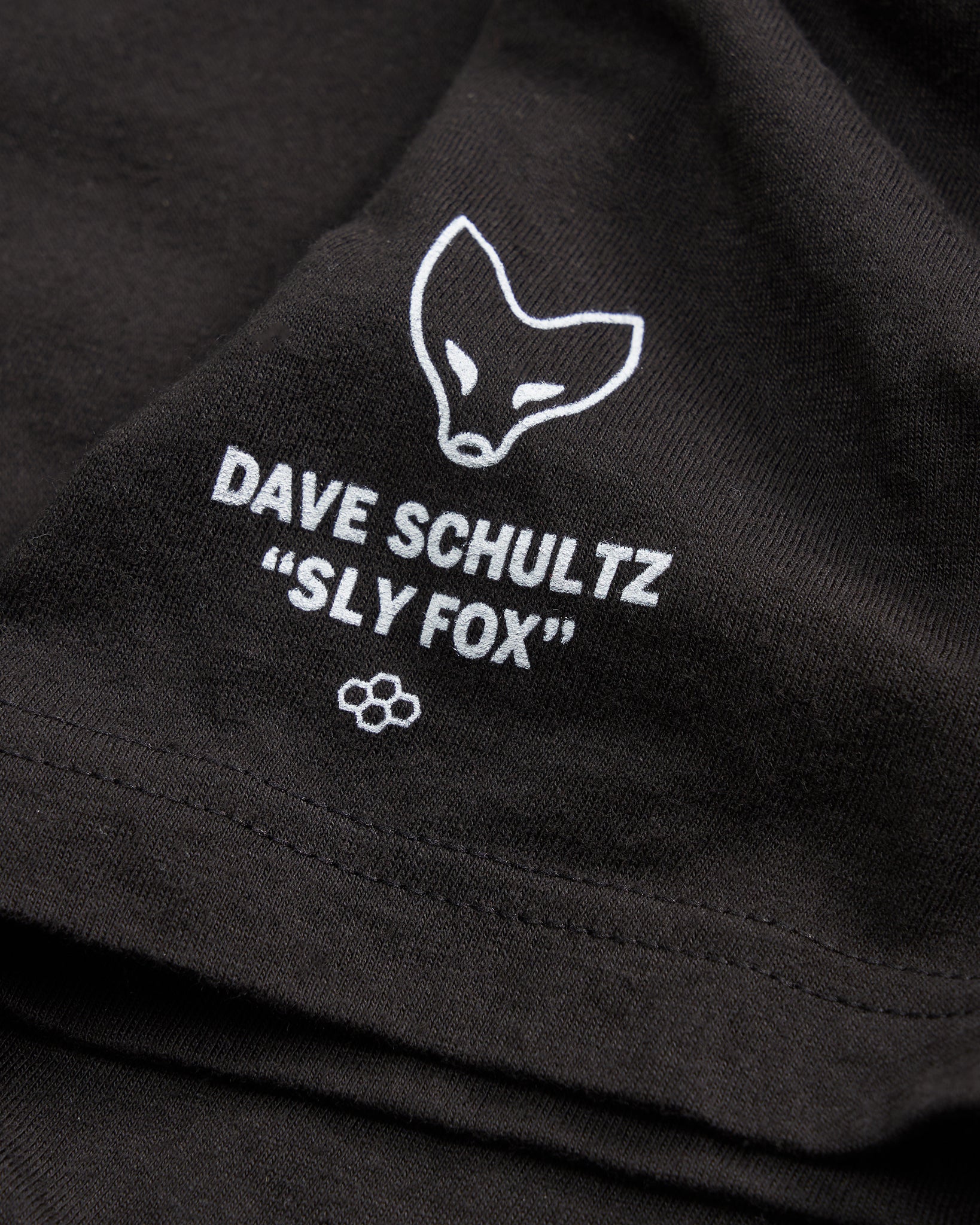 A close-up of a black fabric featuring white printed text and a fox illustration associated with Dave Schultzs Sly Fox