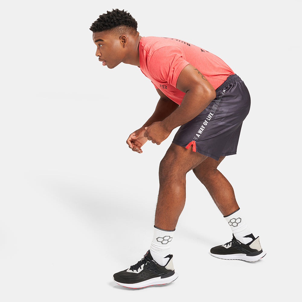 A young male athlete is captured in a dynamic pose wearing red athletic attire and black shorts demonstrating an active stance while preparing for a workout