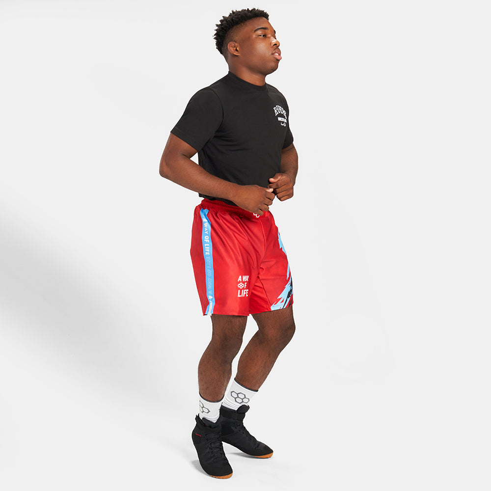 A young man in a black t-shirt and red athletic shorts is captured mid-action showcasing a dynamic pose and stylish sportswear ensemble