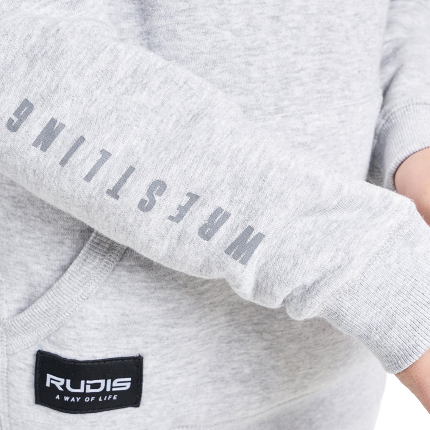 A close-up view of a light gray sweatshirt sleeve featuring the word WRESTLING printed vertically in bold gray letters and a black label for the brand RUDIS