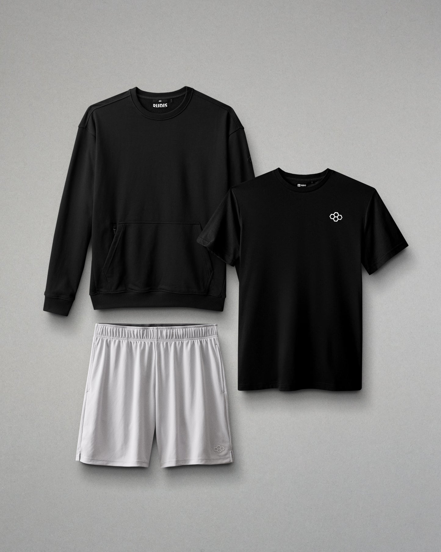 Black sweatshirt, black t-shirt with a logo, and gray shorts on a gray background