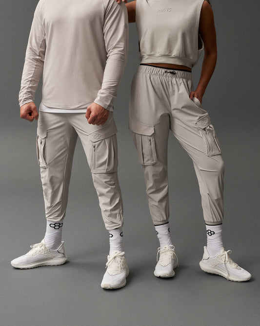 Two people wearing matching light gray outfits on a dark gray background