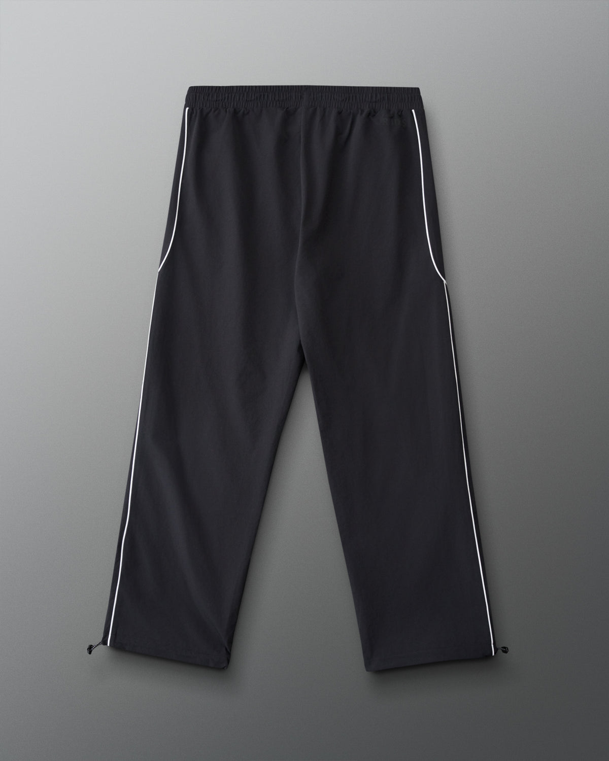 Back view of RUDIS Movement Podium Pants in black with white side piping, relaxed-leg silhouette, and adjustable ankle hems.