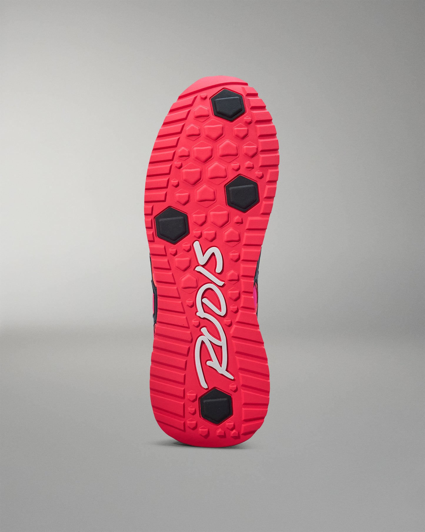 Red and black sole of a shoe with a brand logo on a gray background