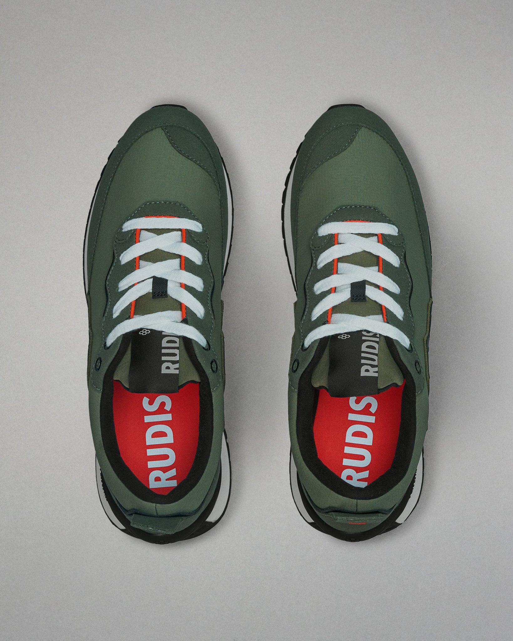 Green sneakers with white laces and red soles on a light gray background