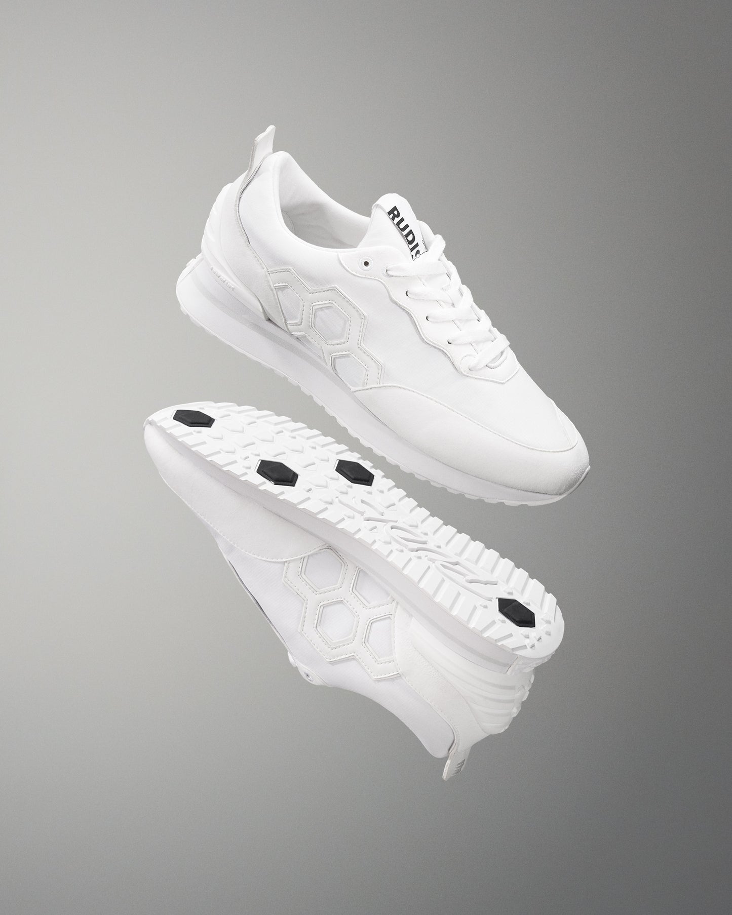 A pair of white RUDIS street lifestyle shoes with a hexagonal pattern on the upper and distinct outsole drive points.