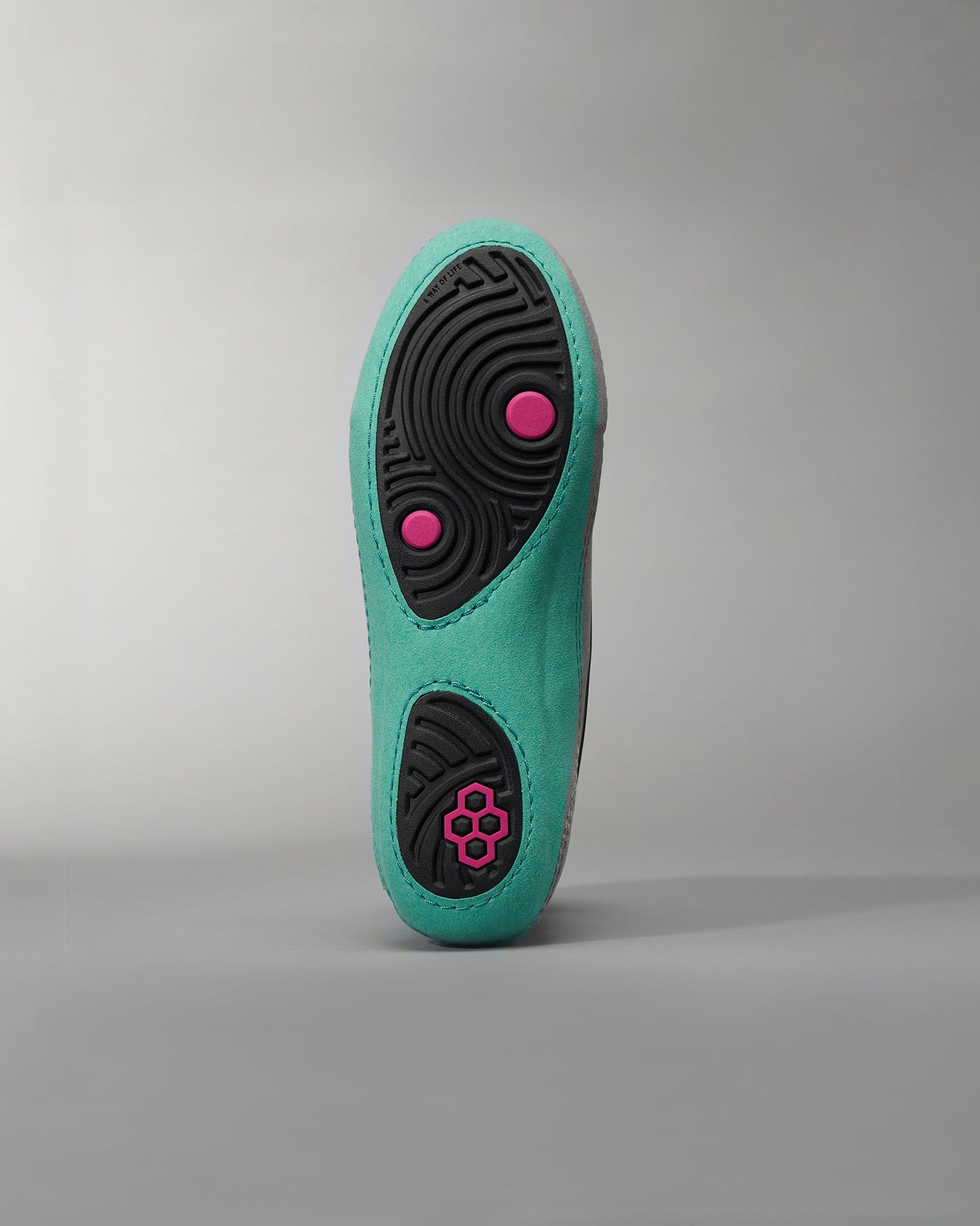 A close-up view of the sole of a vibrant aqua-colored athletic shoe featuring a textured black rubber grip with pink accent details