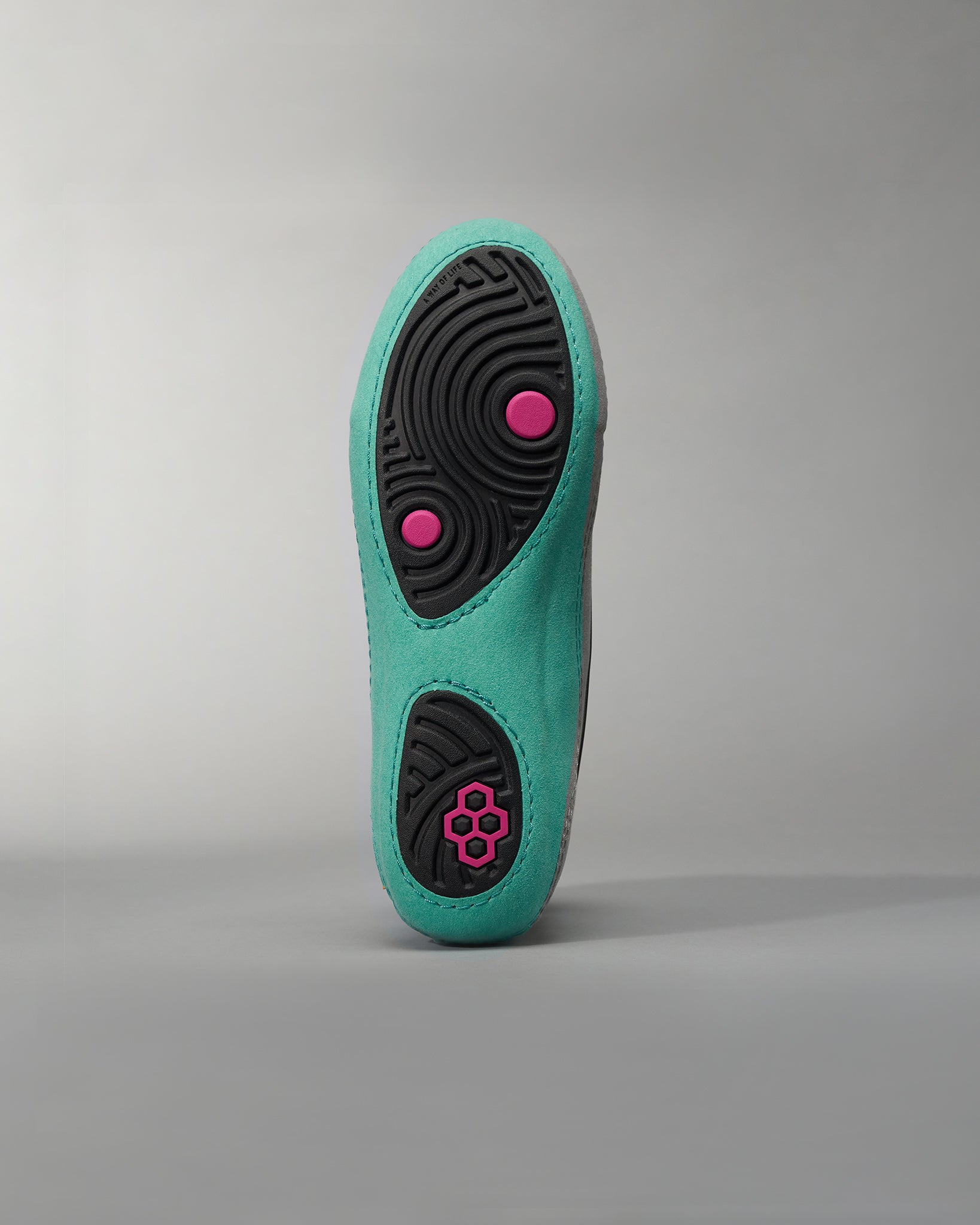 A close-up view of the sole of a vibrant aqua-colored athletic shoe featuring a textured black rubber grip with pink accent details