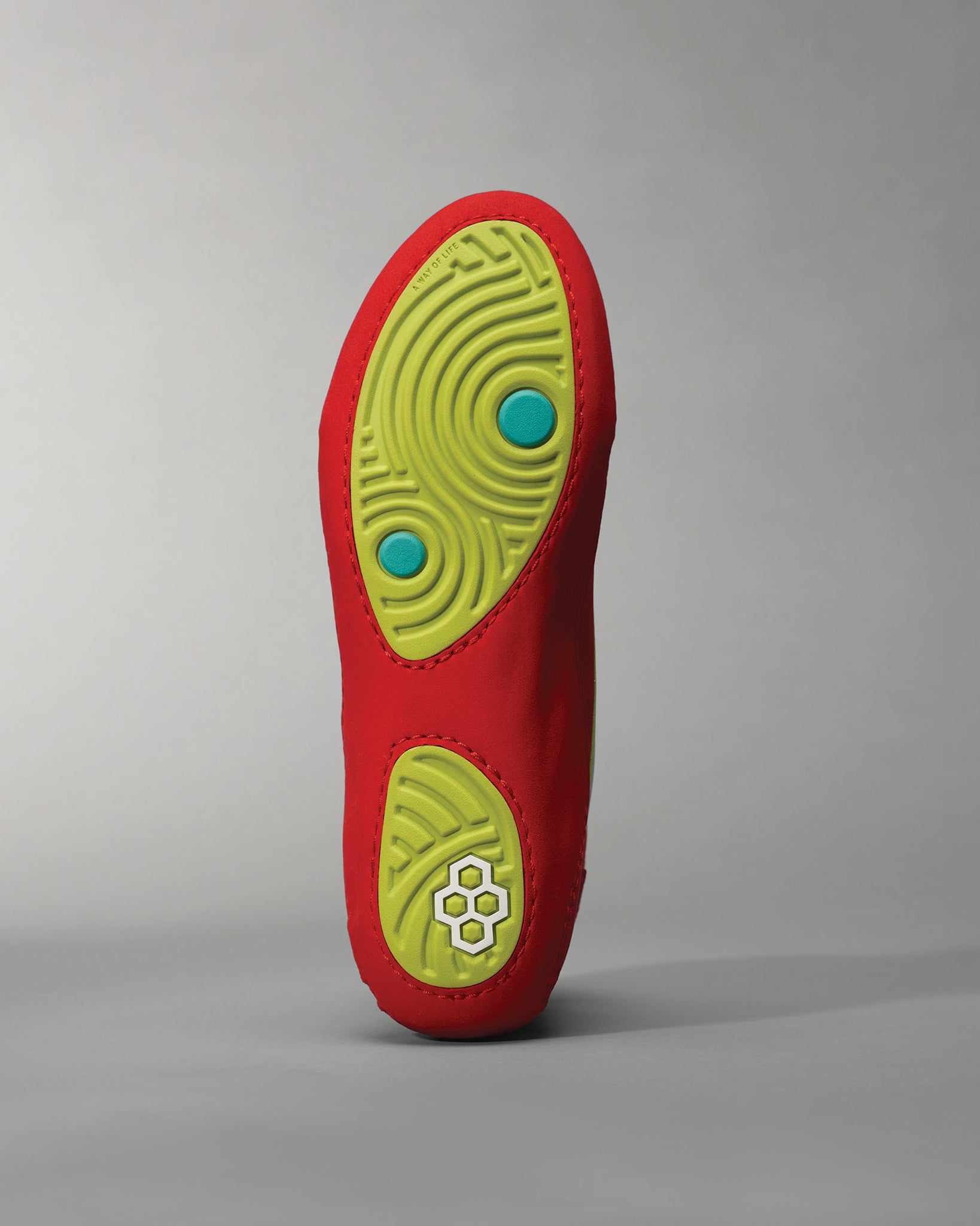 A red athletic shoe sole with a bright green tread pattern and two blue accents featuring a unique design for optimal traction and support