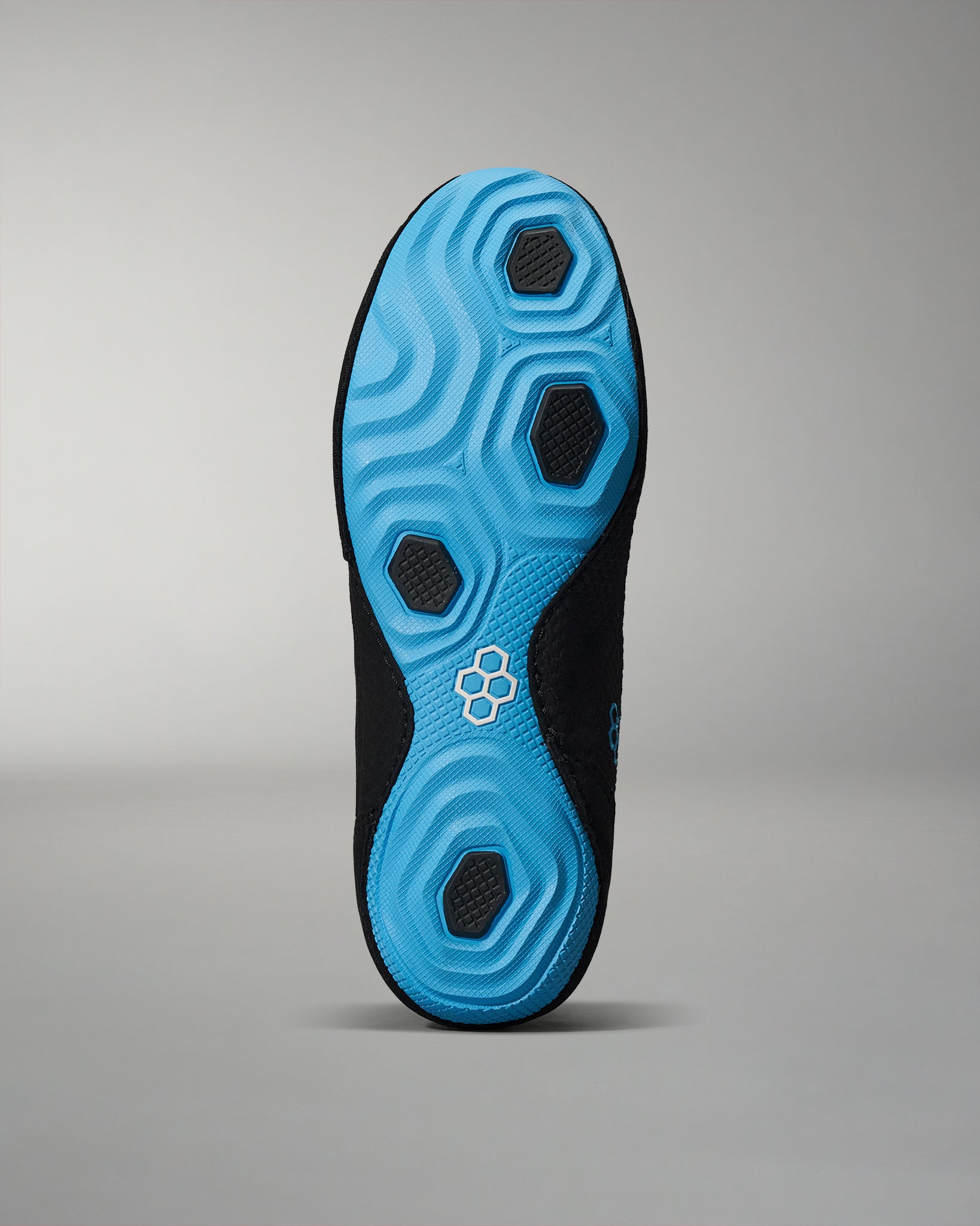 The underside of a shoe features a predominantly light blue design with black textured grip areas, showcasing smooth and wavy patterns against a neutral gray background.