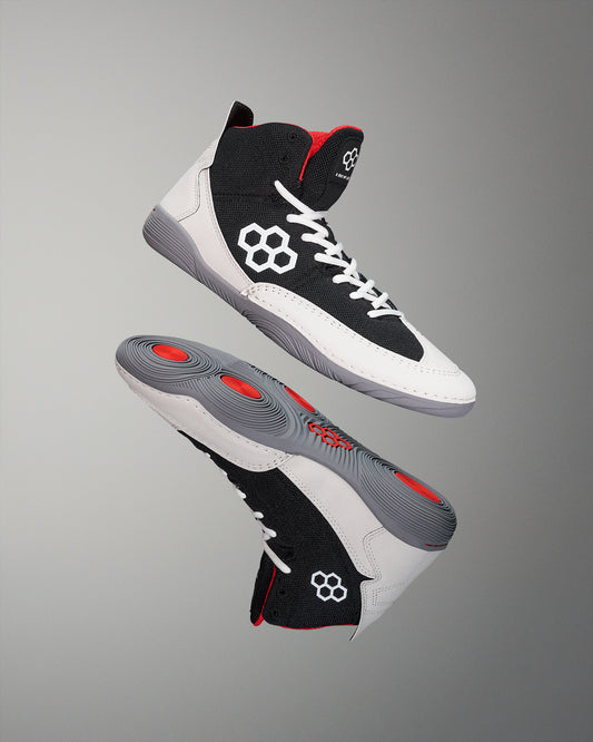 A pair of adult wrestling shoes with black, white, and red colors, featuring a micro-suede rand, and wrapped outsole.