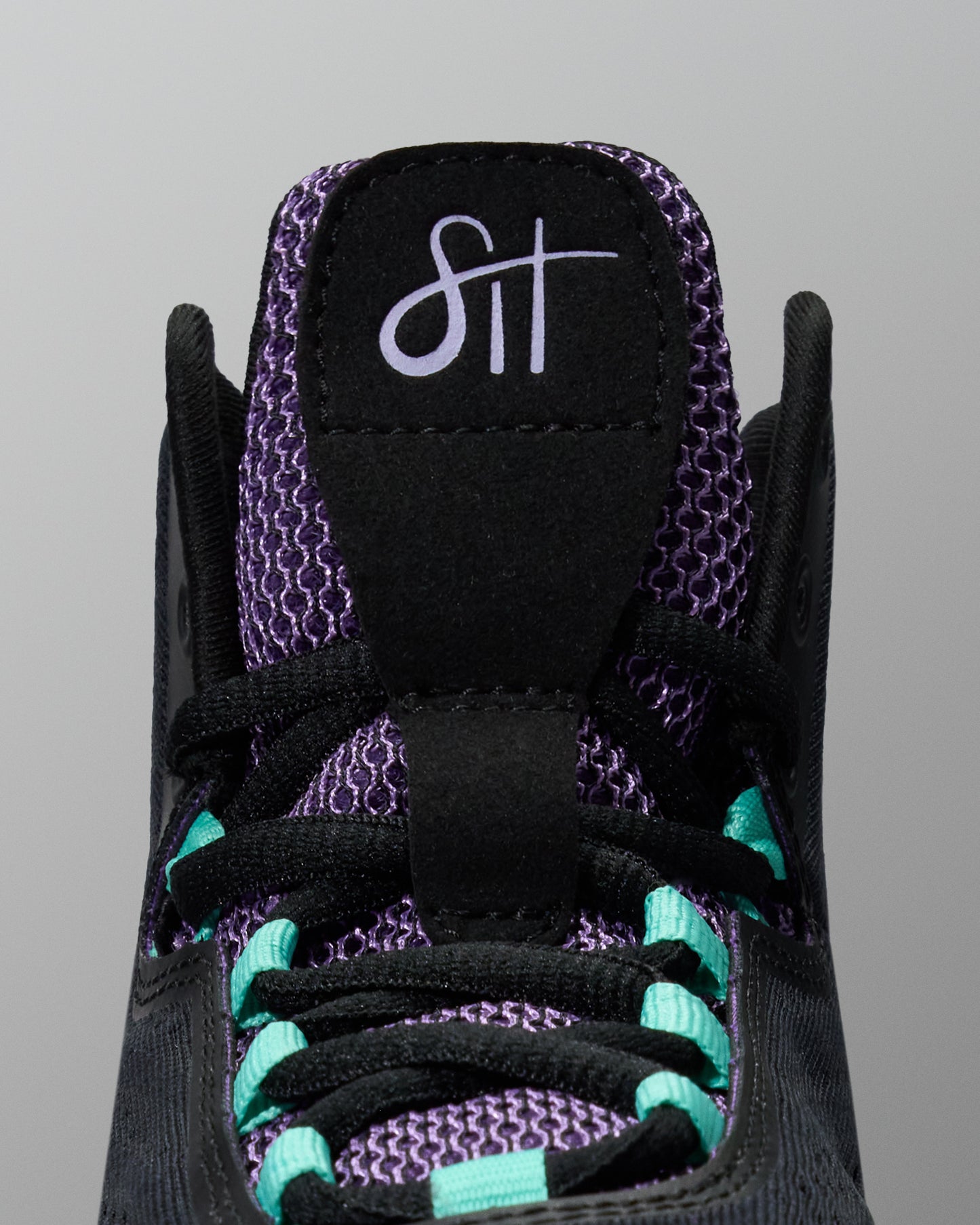 Close-up of a black sneaker with purple and teal accents on a gray background