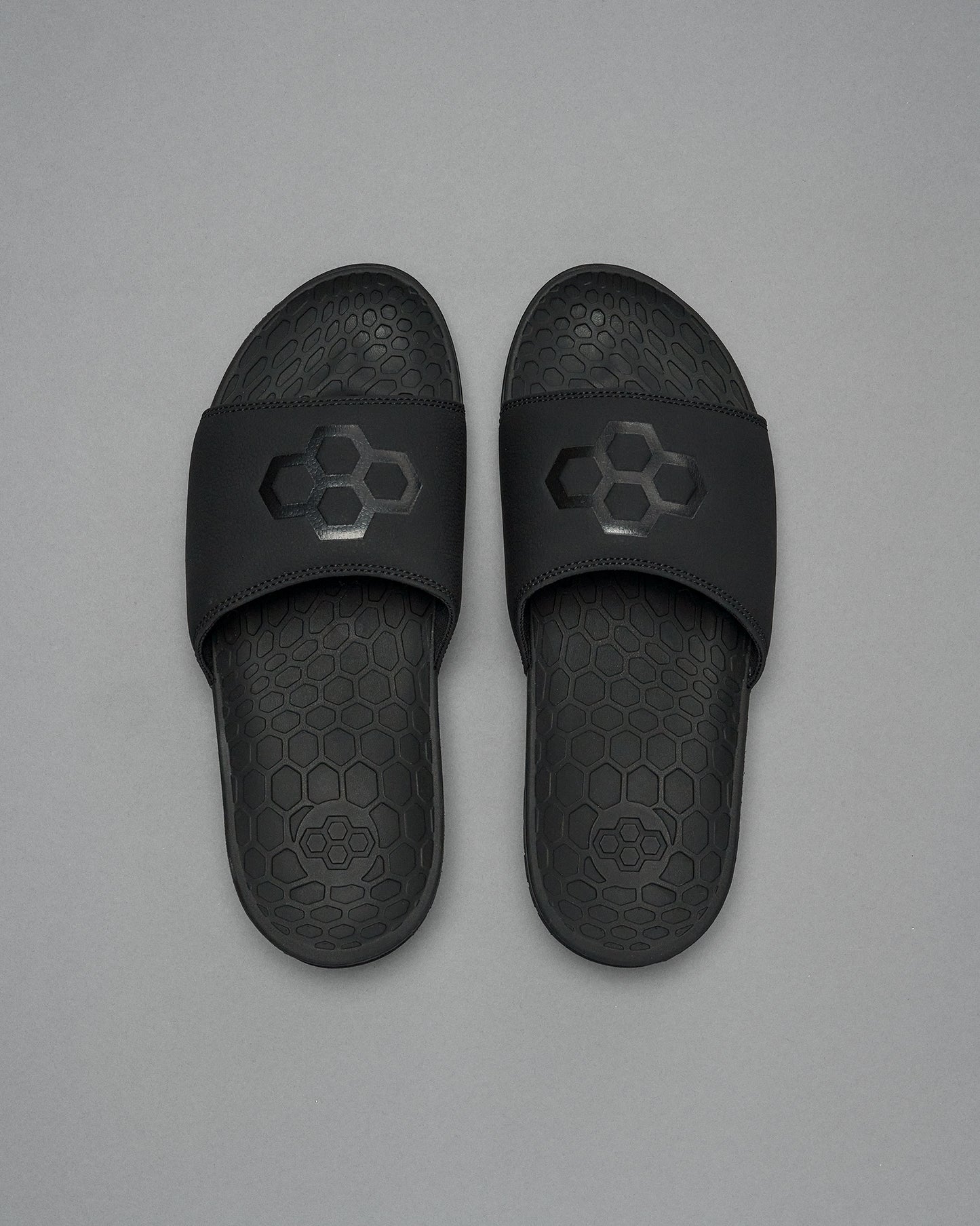 A pair of black RUDIS Hex slides with the brand's logo on the strap, placed on a grey background.