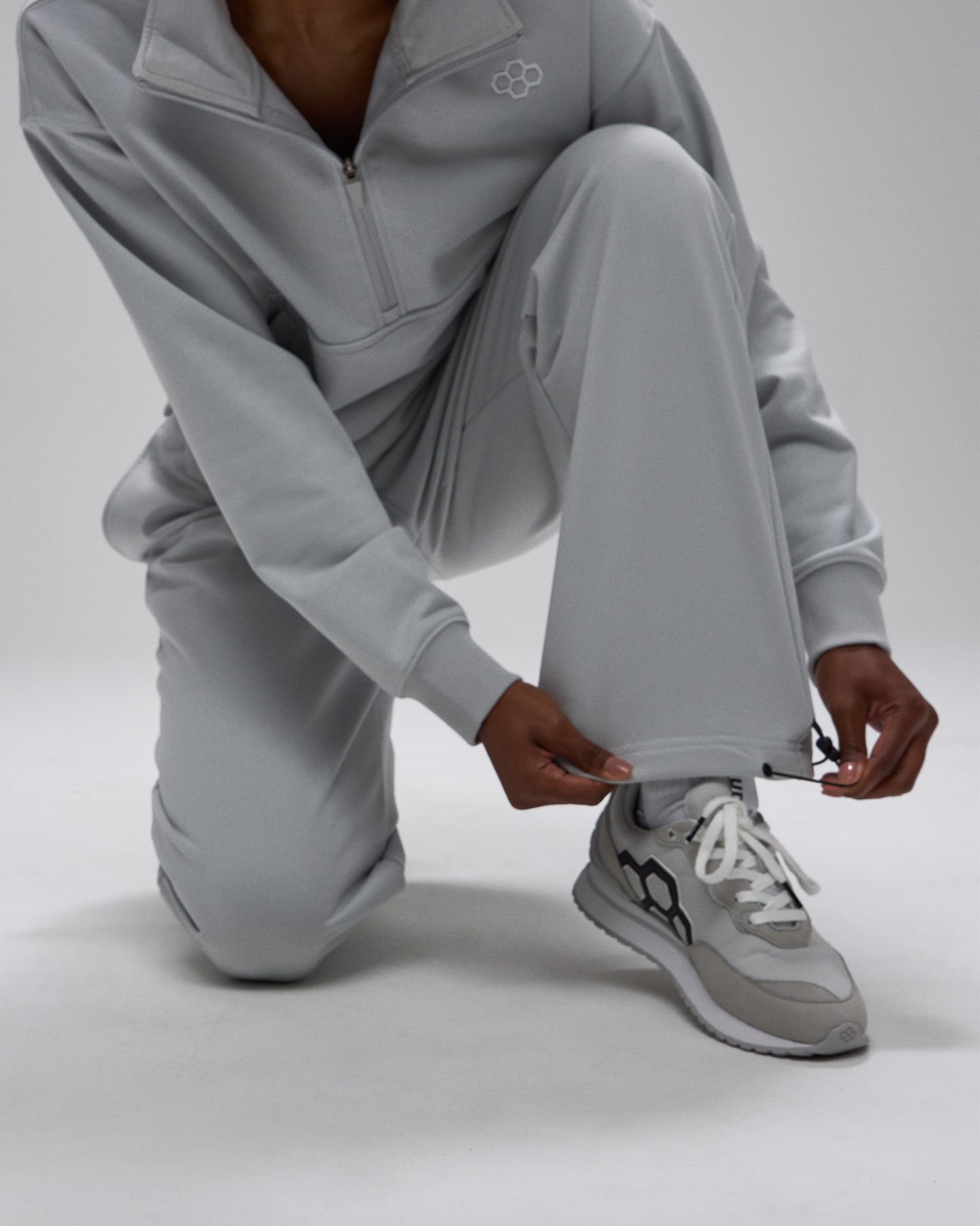 Person wearing a gray tracksuit with matching sneakers on a light gray background