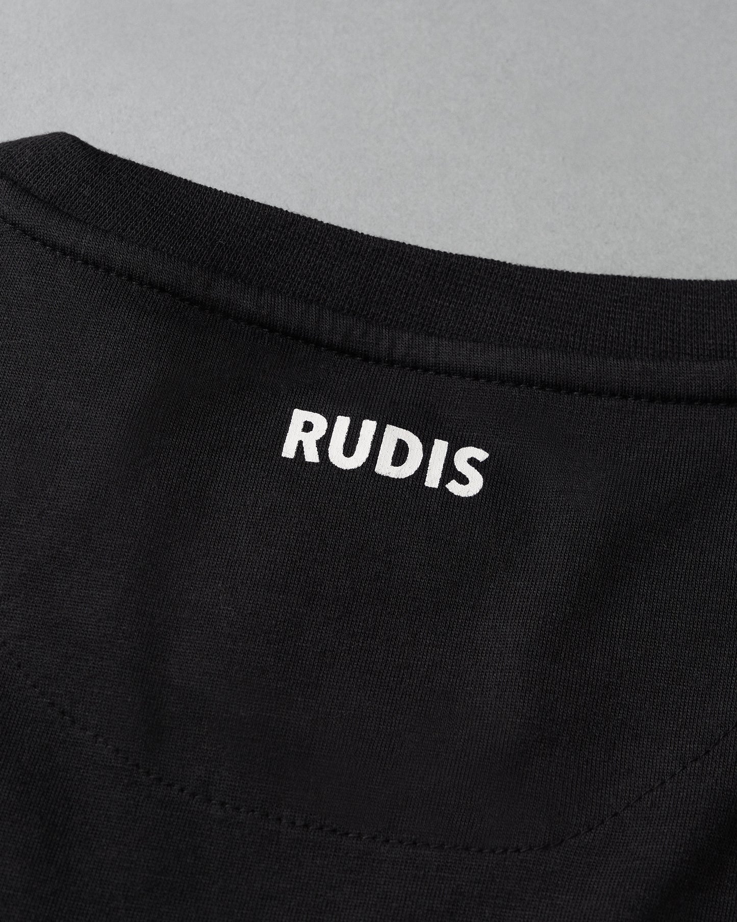 Close-up of a black garment with 'RUDIS' branding on a gray background