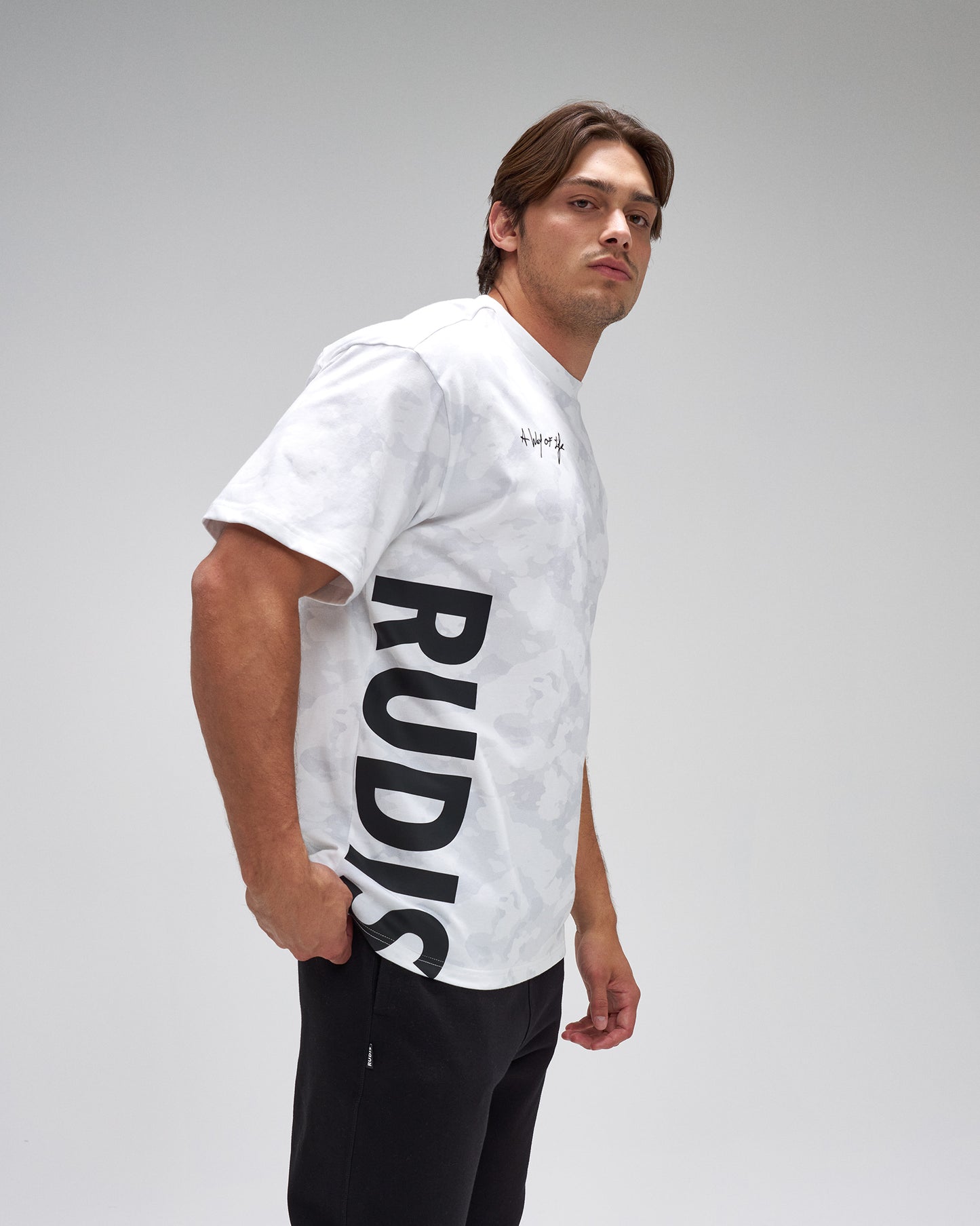 Man wearing a white t-shirt with 'RUDIS' logo on a gray background