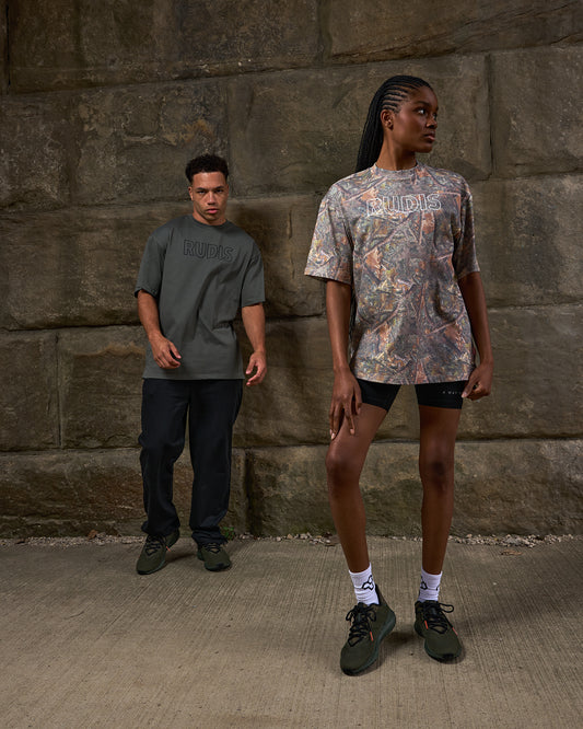 Two people standing against a stone wall, wearing branded t-shirts.