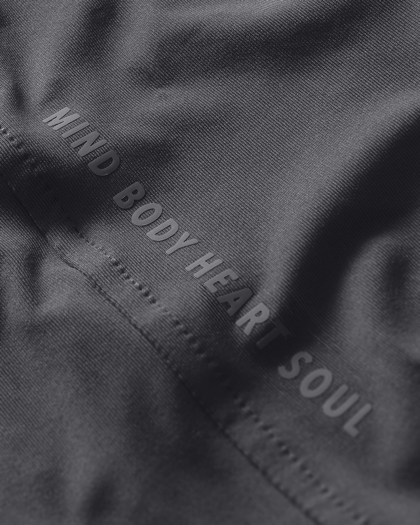 Text 'MIND BODY HEART SOUL' embroidered on a dark fabric background