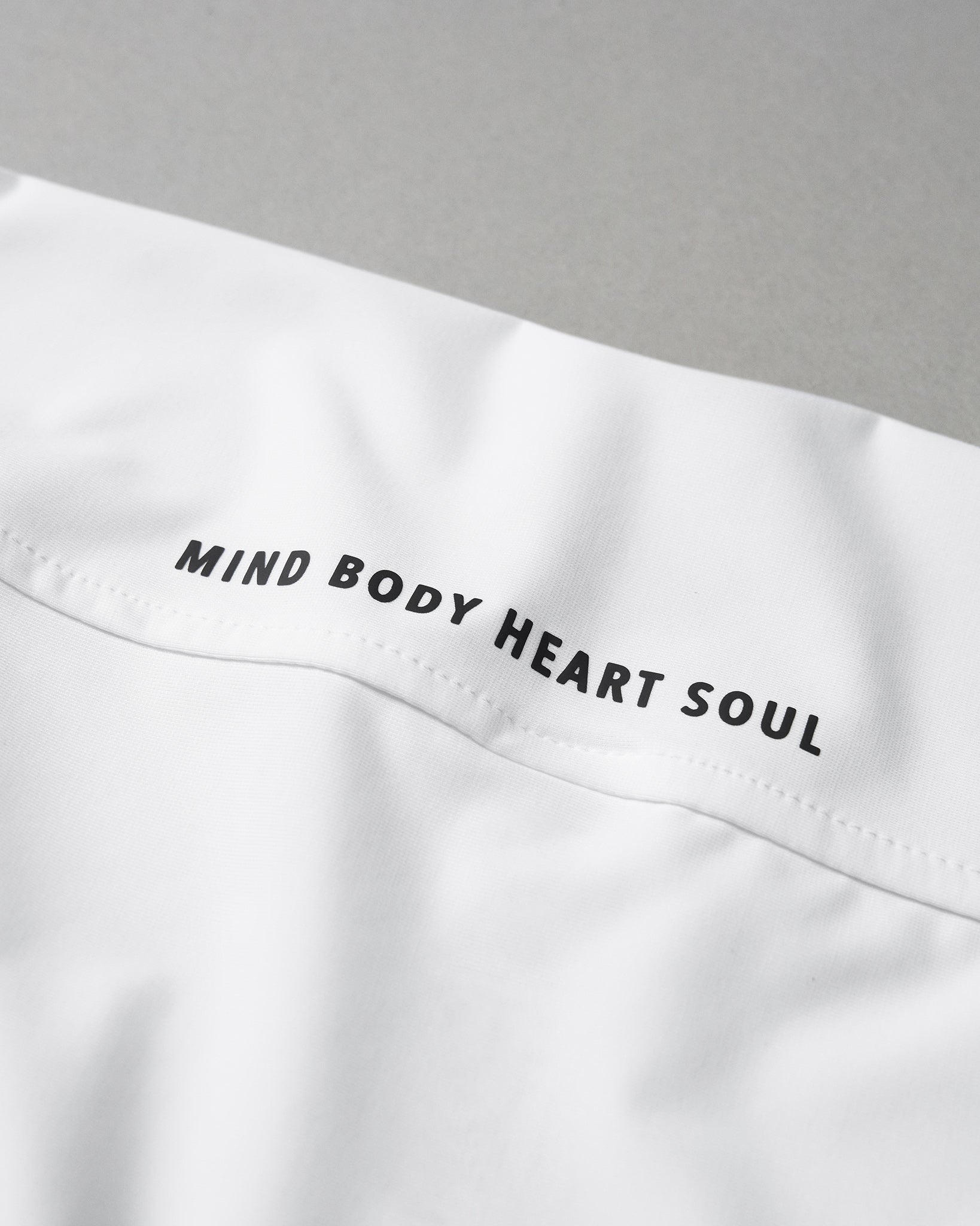 White garment with 'MIND BODY HEART SOUL' text on a gray background