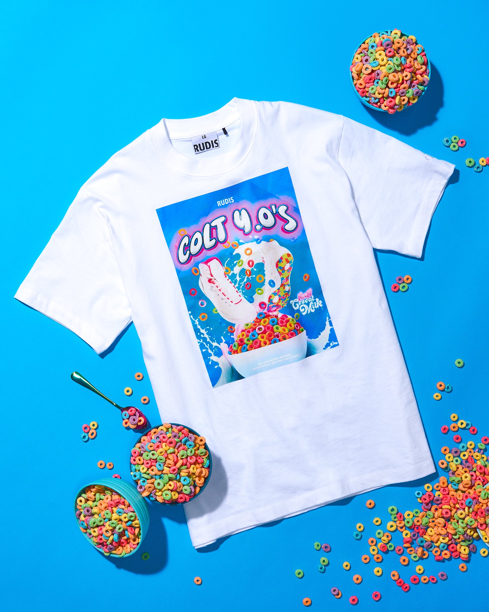White t-shirt with a colorful graphic design on a blue background with cereal bowls.