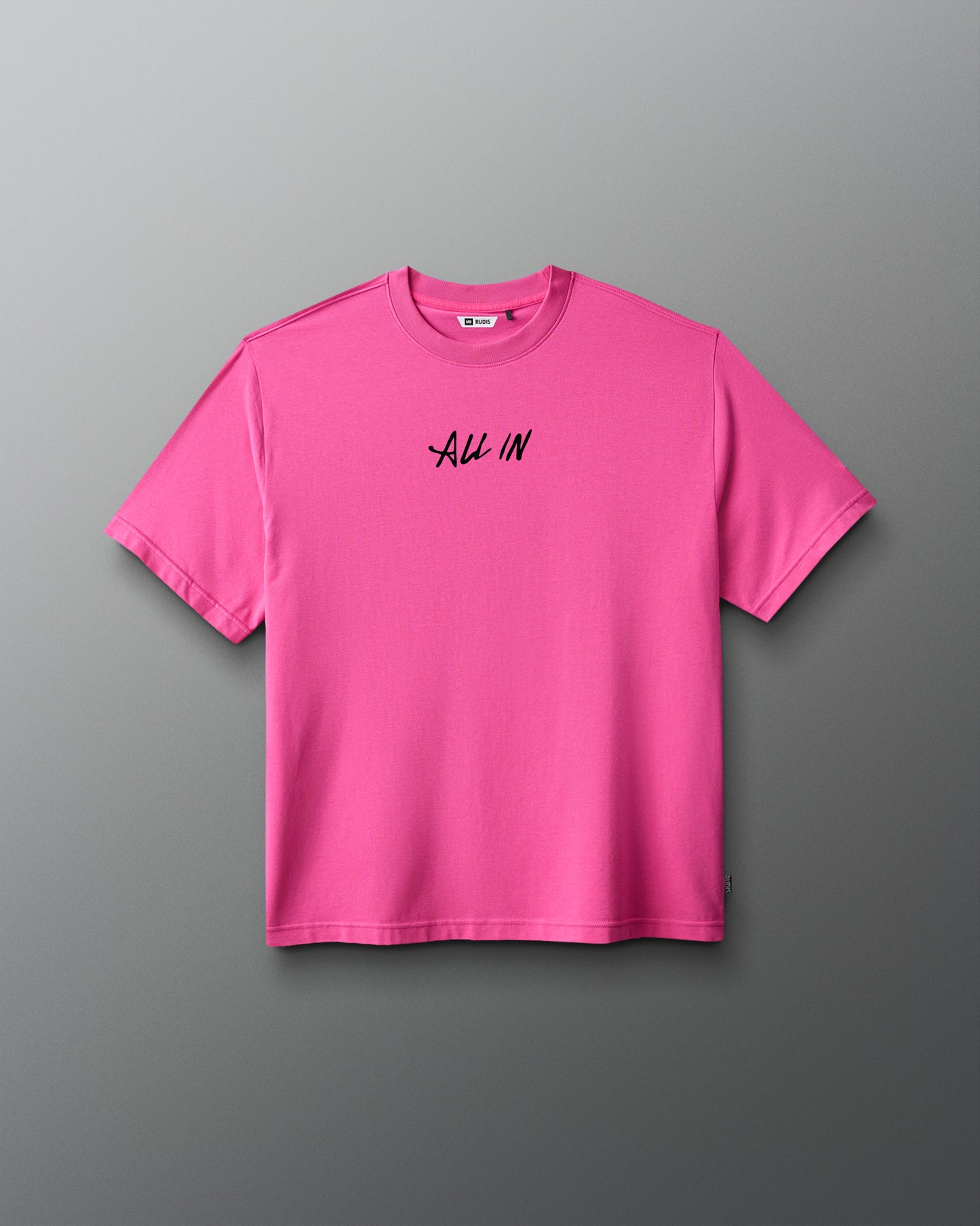 A bright pink short-sleeve crewneck t-shirt with the words 'ALL IN' printed in black script across the chest, displayed against a dark gray gradient background.