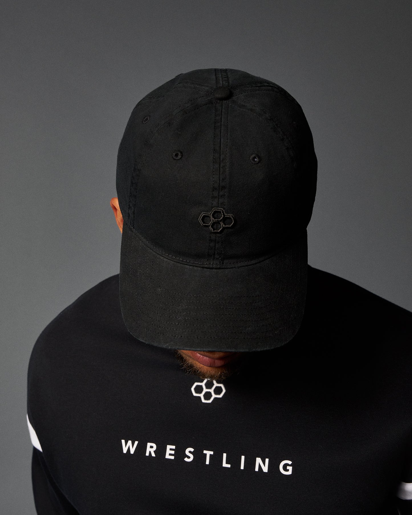 Person wearing a black cap and black 'Wrestling' shirt on a gray background