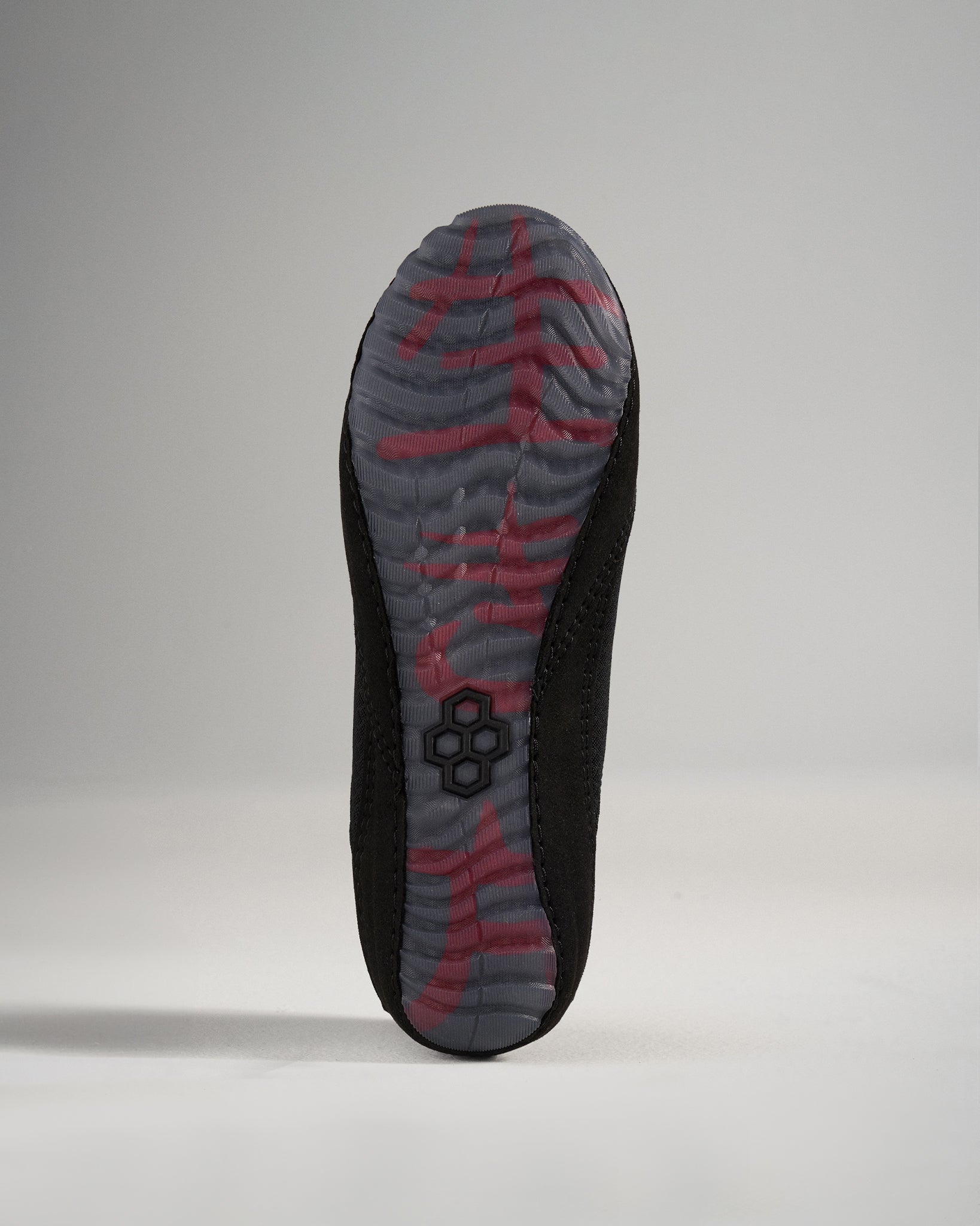 The image displays the sole of a black athletic shoe featuring a textured tread and dynamic design elements in gray and red colors