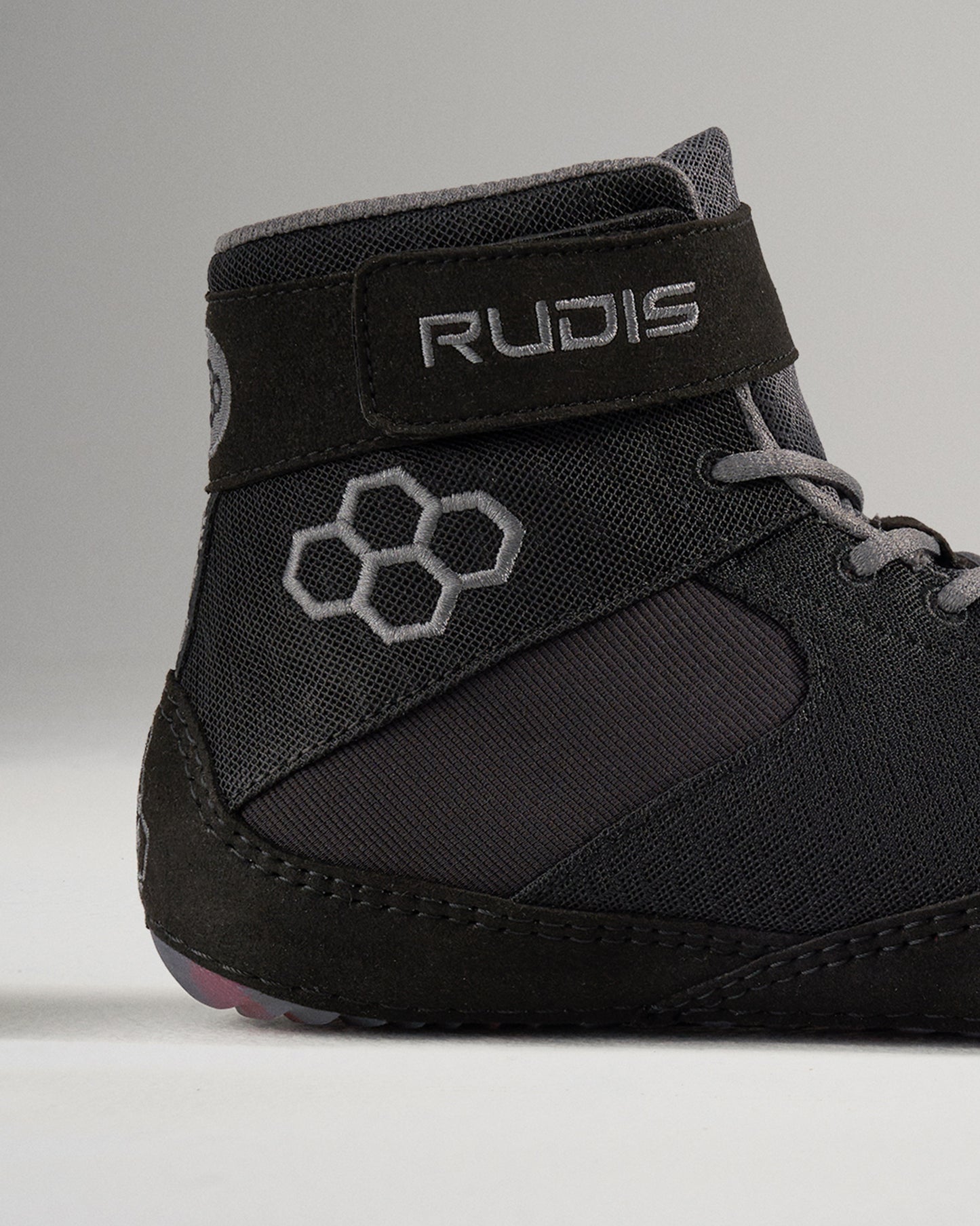 This image features a close-up of a black wrestling shoe from Rudis showcasing its modern design and unique logo elements
