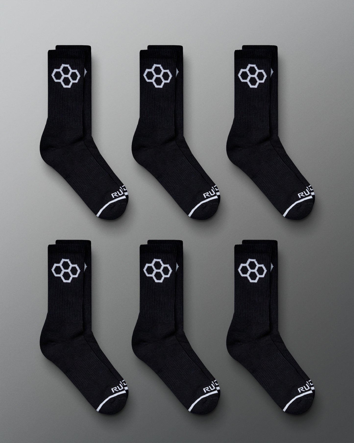 A display of six pairs of black athletic socks featuring a distinctive white hexagonal logo and stylish design details laid out on a gray background