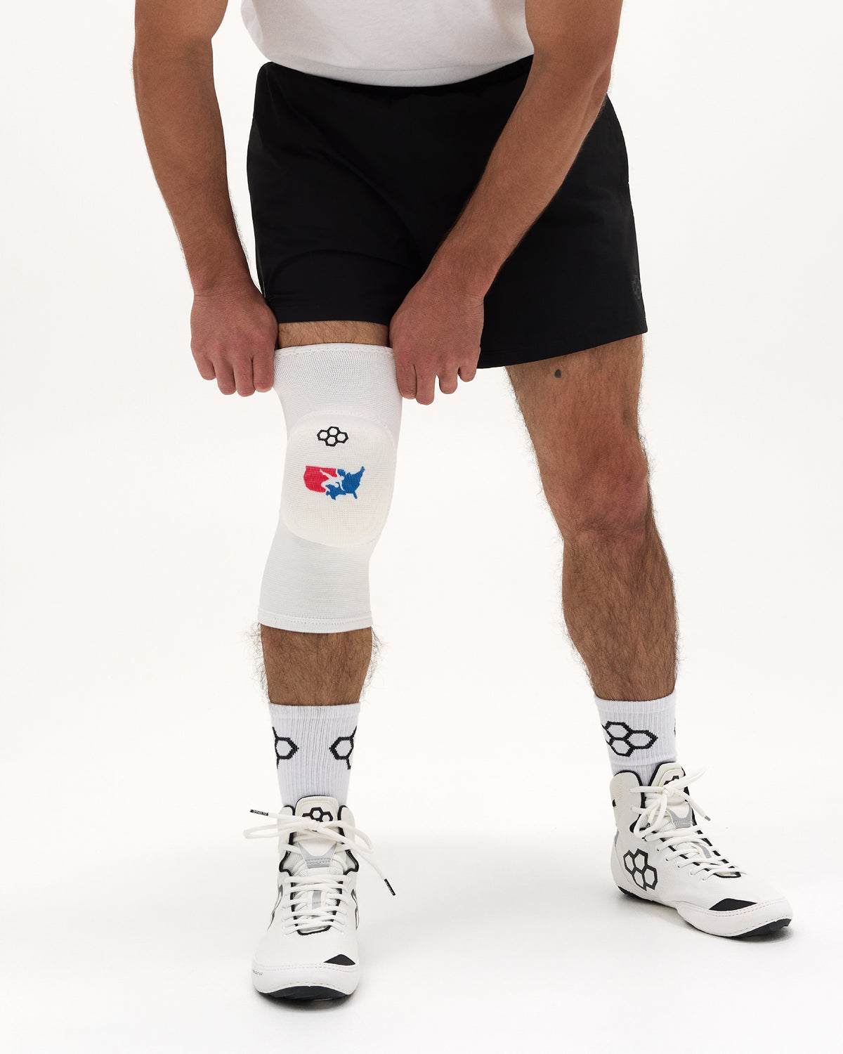 RUDIS USA Wrestling Map Cushion Knee Pad in white shown on a wrestler adjusting the sleeve above the knee.