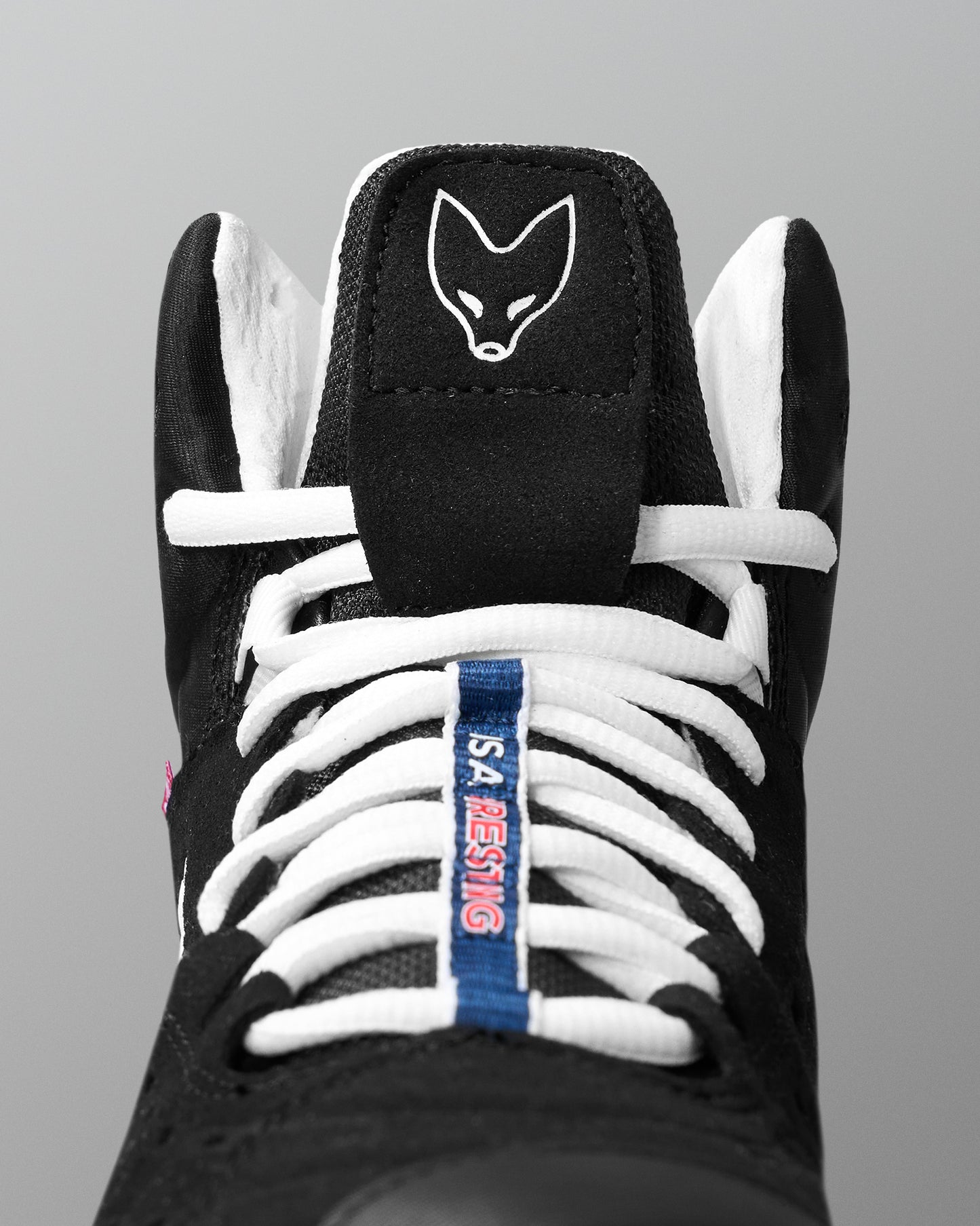 Black wrestling shoe with white laces and a blue tag on a gray background