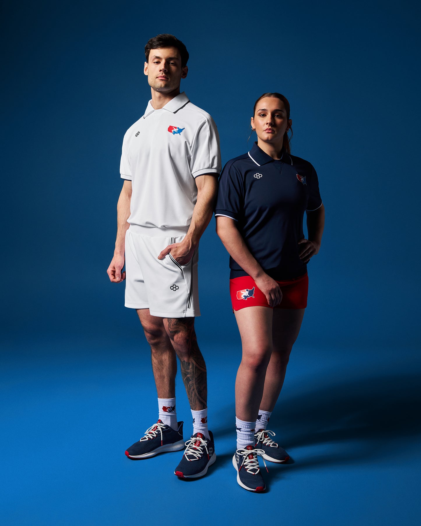 A male and a female wrestler standing side by side wearing USA Wrestling polos in white and blue colors, with the male in the foreground and the female in the background.
