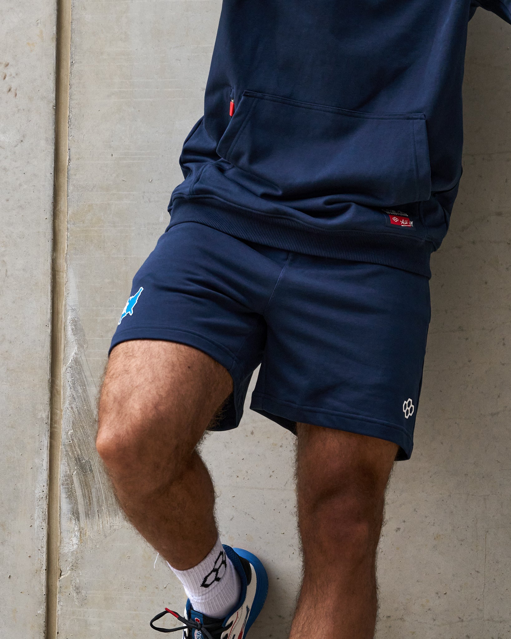 Person wearing navy athletic shorts and a shirt against a concrete wall.