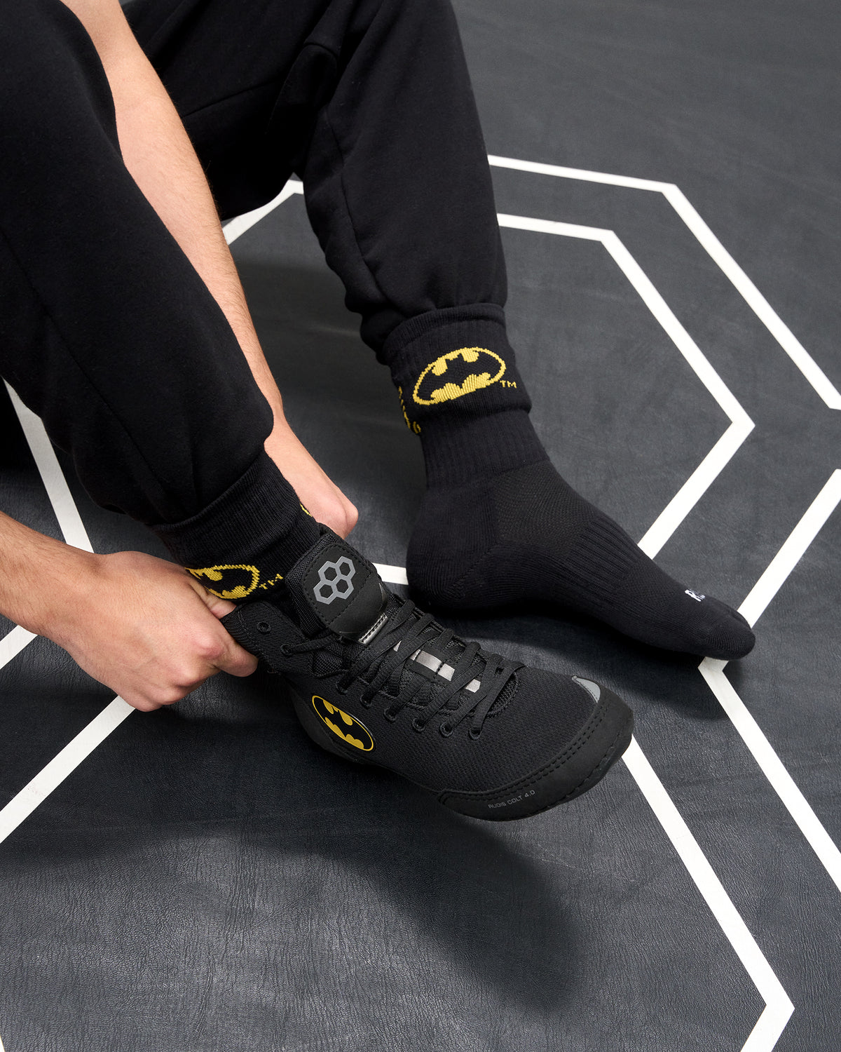 Wrestler wearing black RUDIS Batman Cushion Crew Socks with yellow Batman logos while putting on a black Batman wrestling shoe.