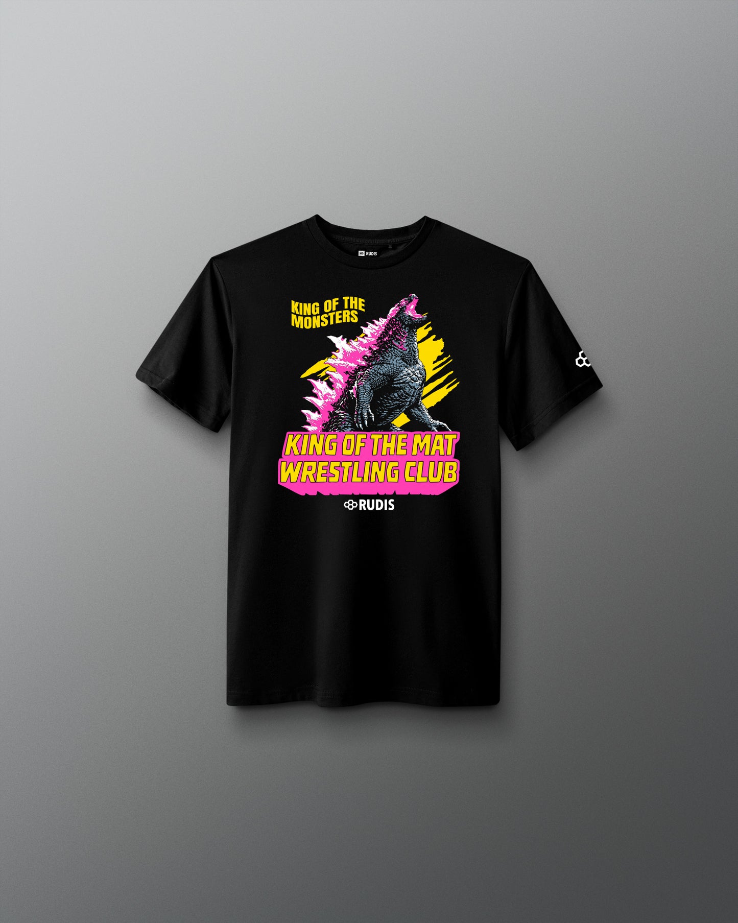 A black short-sleeve graphic t-shirt displayed flat against a dark gray gradient background. The shirt features a colorful front print of Godzilla with the text 'King of the Mat Wrestling Club' in yellow and pink, and a small white logo on the right sleeve.