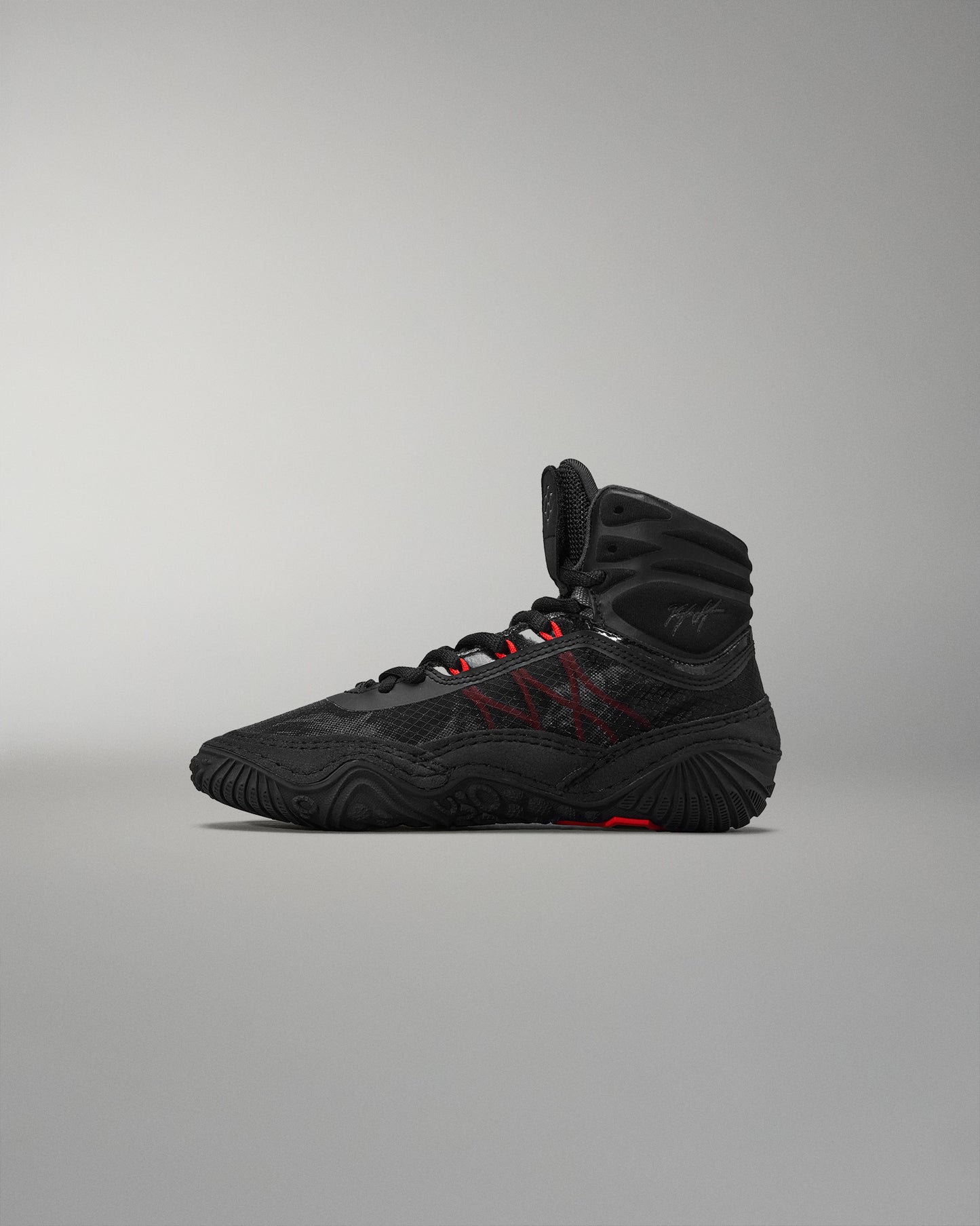 High-top athletic shoe shown in black with red accents and a textured surface for grip, set against a neutral gray background.