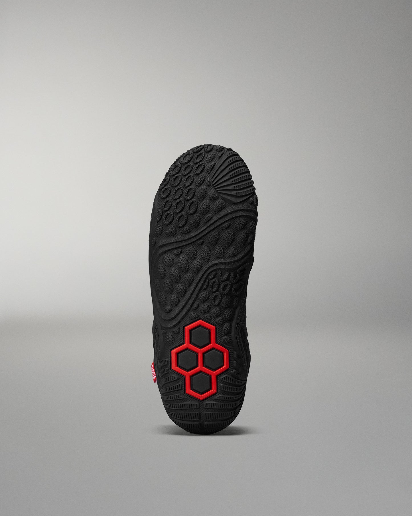 The sole of a shoe exhibits a textured black surface with a central red honeycomb design, framed by a soft gray background.