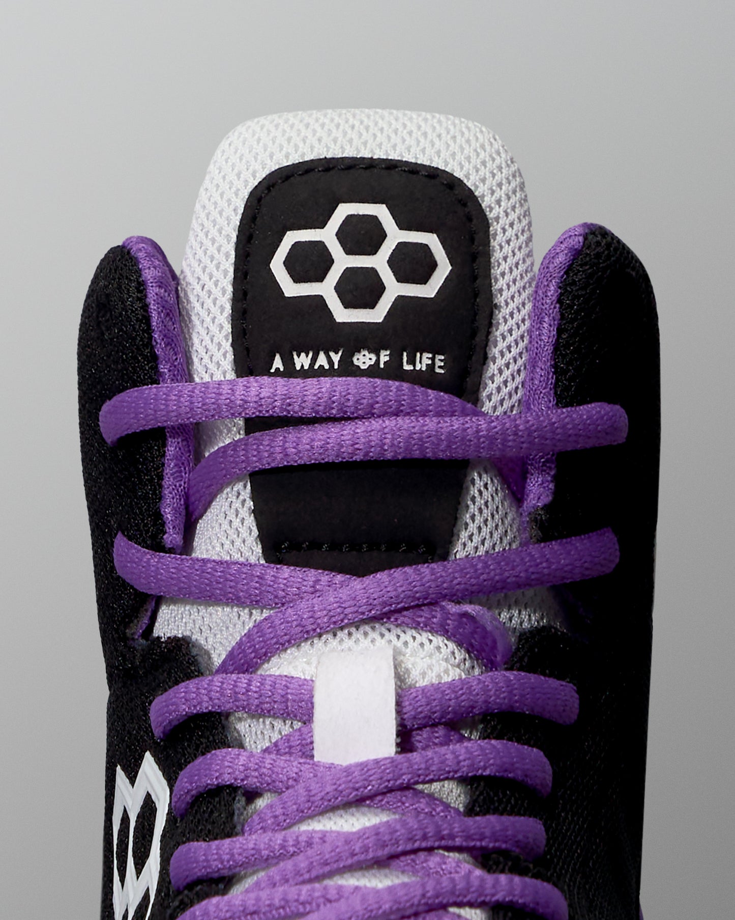 Close-up of a sneaker with purple laces and black and white accents on a gray background
