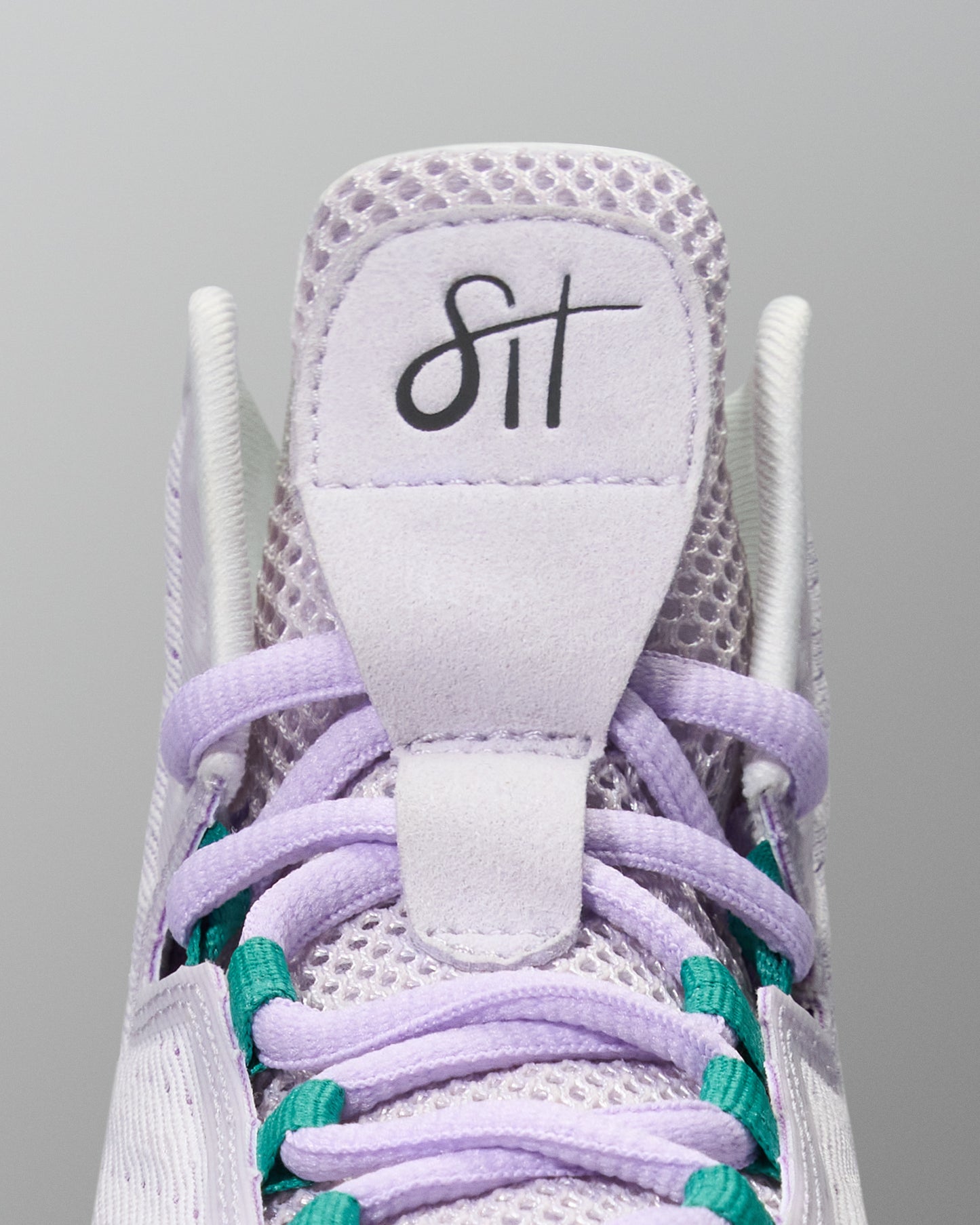 Close-up of a sneaker with purple laces and a visible brand logo on a gray background
