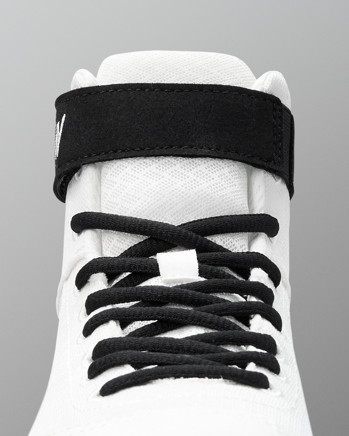 White wrestling shoe with black shoelaces on a gray background