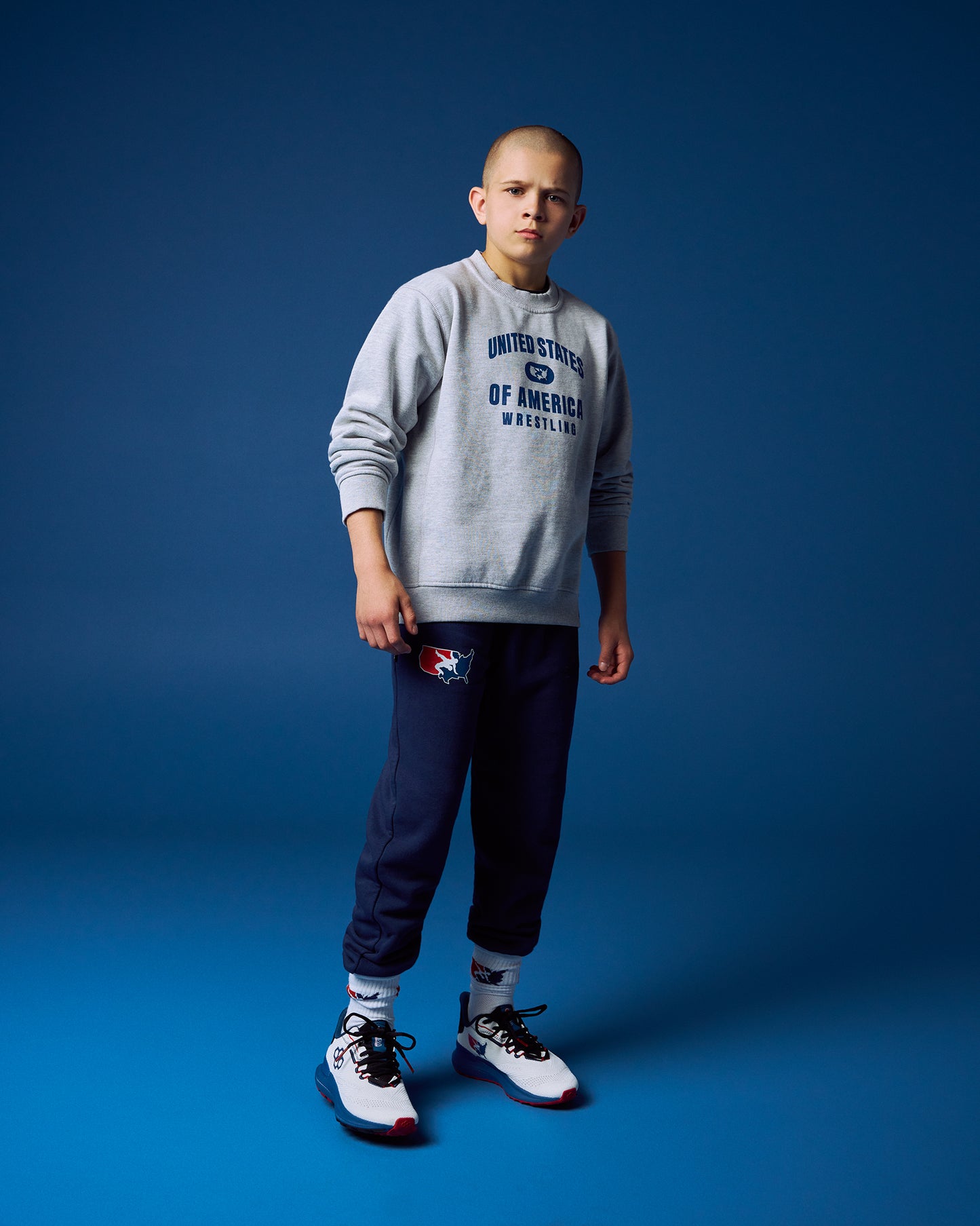 Person wearing a gray sweatshirt with text and dark pants on a blue background