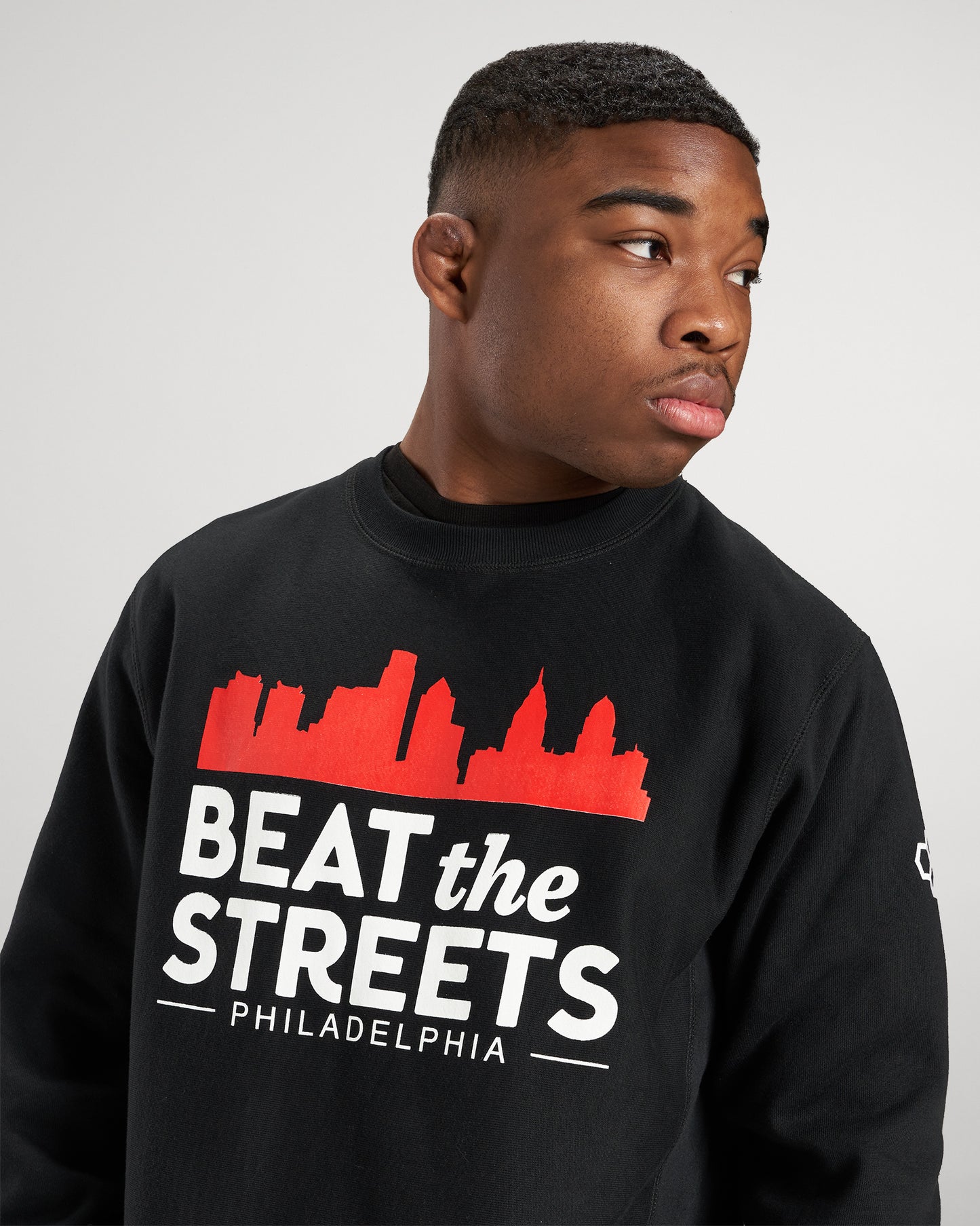 A young man wearing a black sweatshirt with a vibrant design that features the phrase BEAT the STREETS and a silhouette of Philadelphias skyline