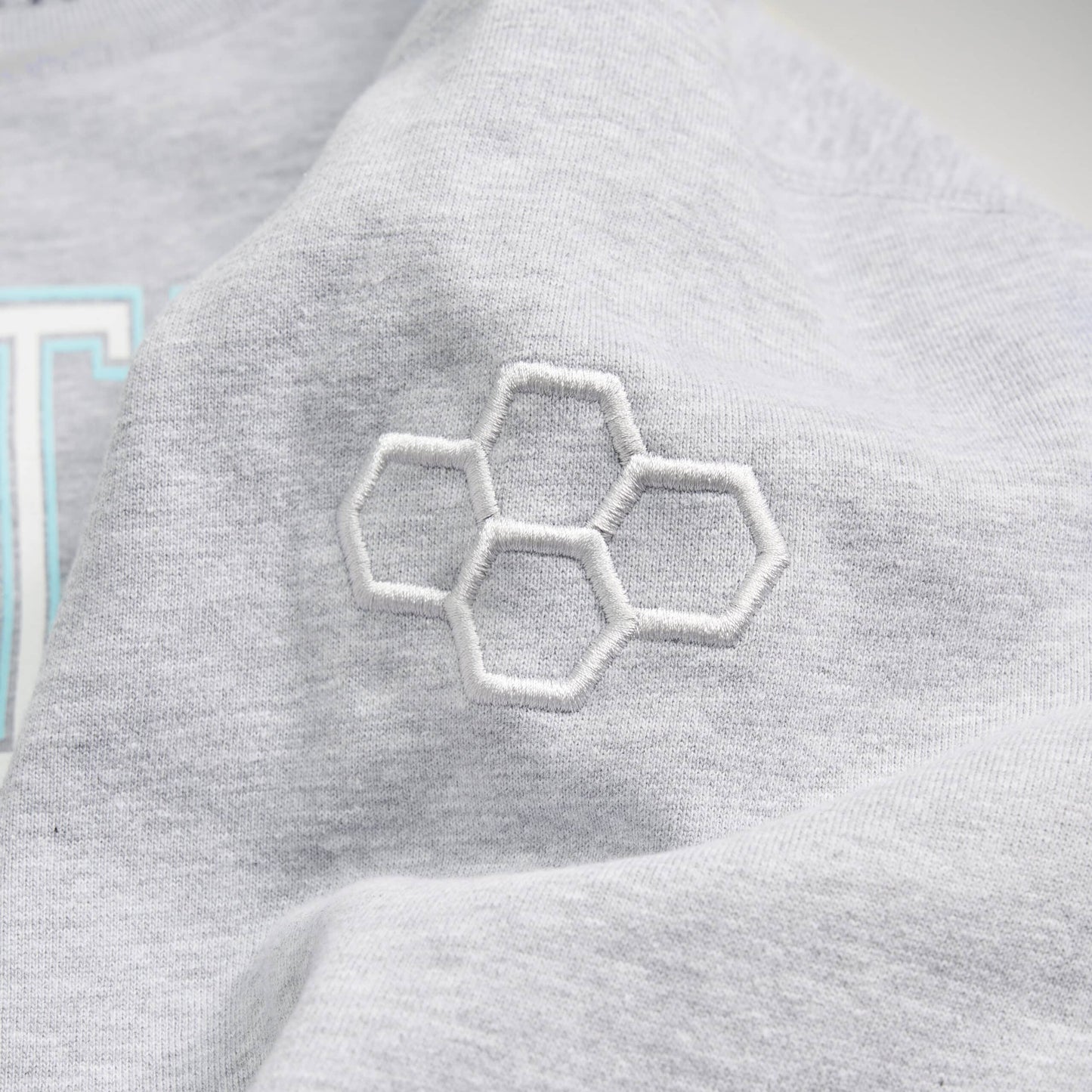 A close-up view of a light gray garment featuring an intricate white embroidered hexagon design on the sleeve