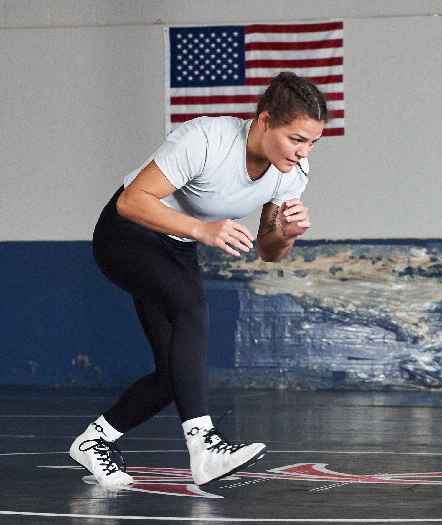 Image of Kayla Miracle in a wrestling room wearing RUDIS wrestling apparel and white International wrestling shoes. 