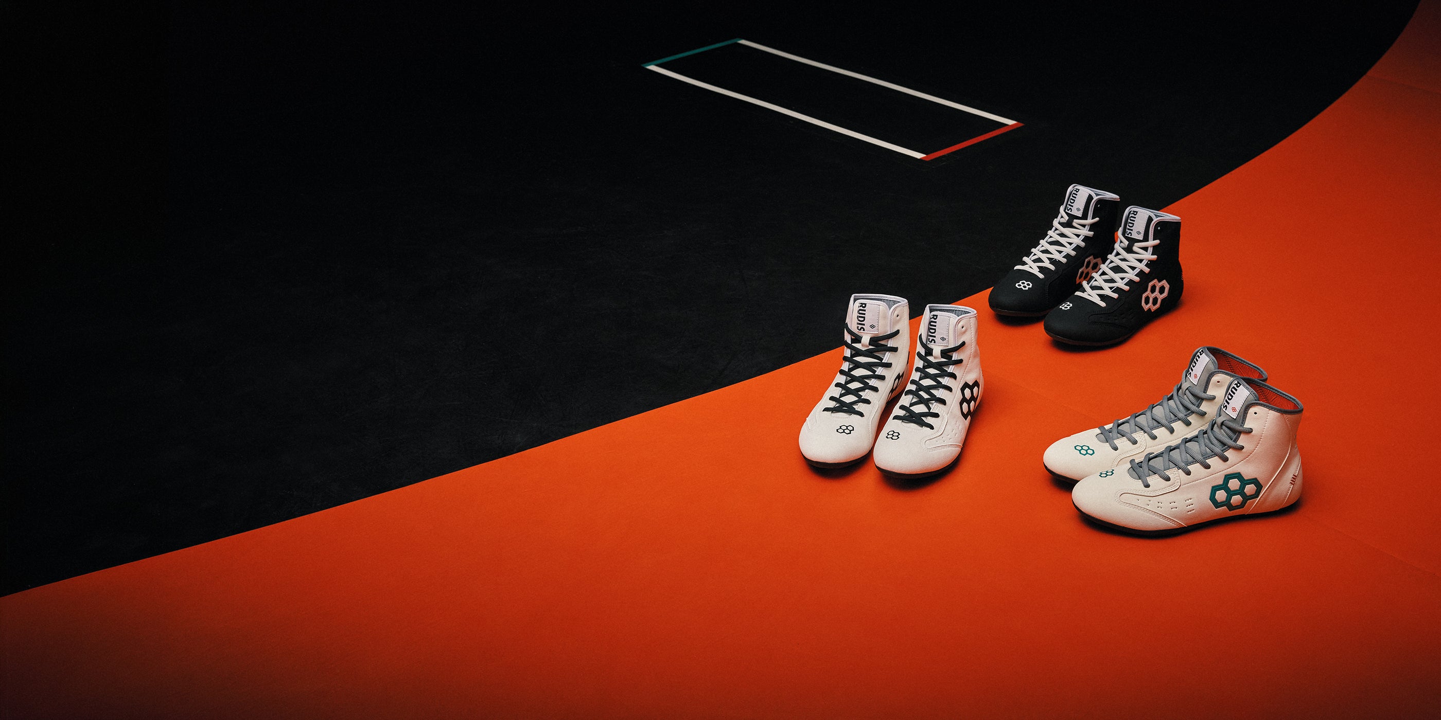 Image of 3 pairs of RUDIS International wrestling shoes sitting on an orange and black wrestling mat. 