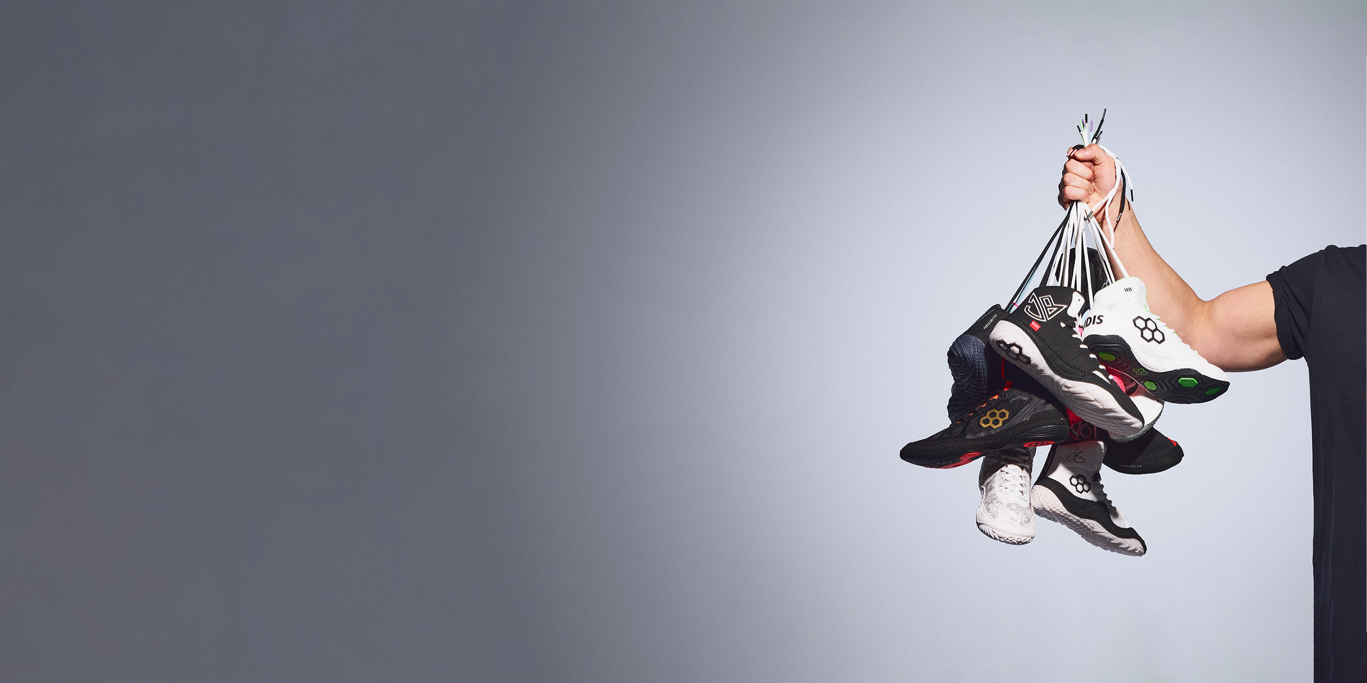 Arm holding multiple pairs of RUDIS wrestling shoes in black and white colorways, showcasing lightweight performance footwear including JB1, JB-UltraLITE and Colt 4.0 models.