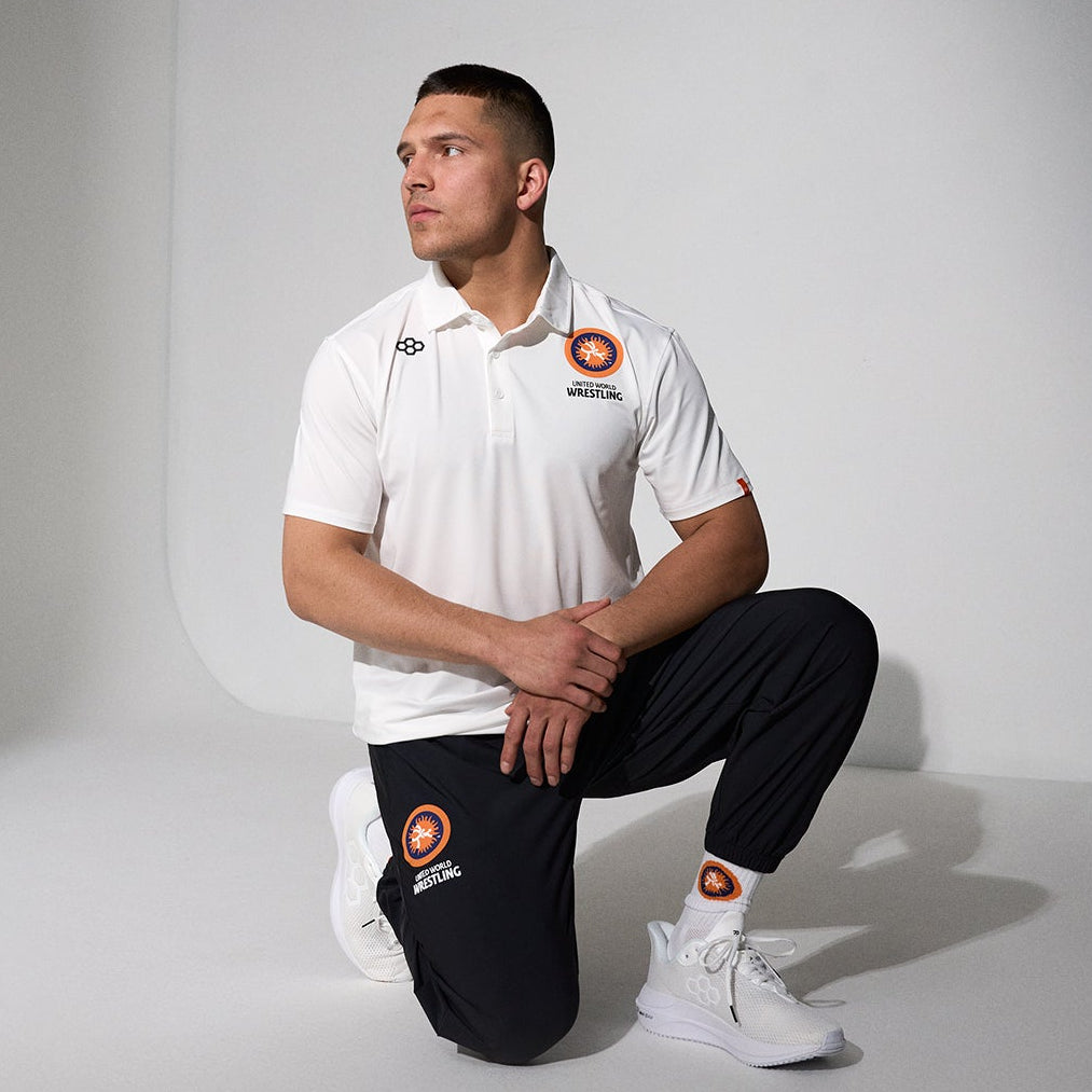 Person wearing a white RUDIS United World Wrestling polo with black RUDIS UWW pants on a plain background